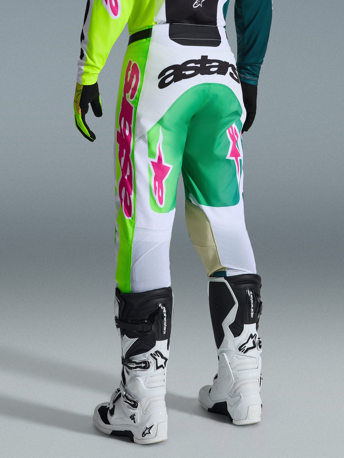 Alpinestars 2026 Racer Portl bukser, motocross-bukser, grøn, hvid og sort med lyserøde detaljer, set bagfra med et fremtrædende 'astars'-logo på sædet og lyserøde stjerne-logoer på benene, kombineret med hvide og sorte motocross-støvler, performance-udstyr til off-road kørsel