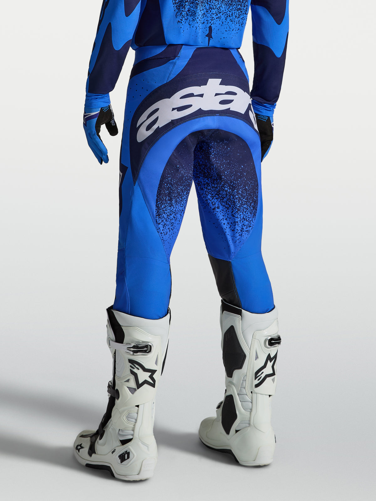 Alpinestars Techstar Swan bukser, herre-motocrossbukser, blå og mørkeblå, set bagfra med stort hvidt logo på sædet, båret med hvide motocrossstøvler, optimeret til MX og off-road kørsel.