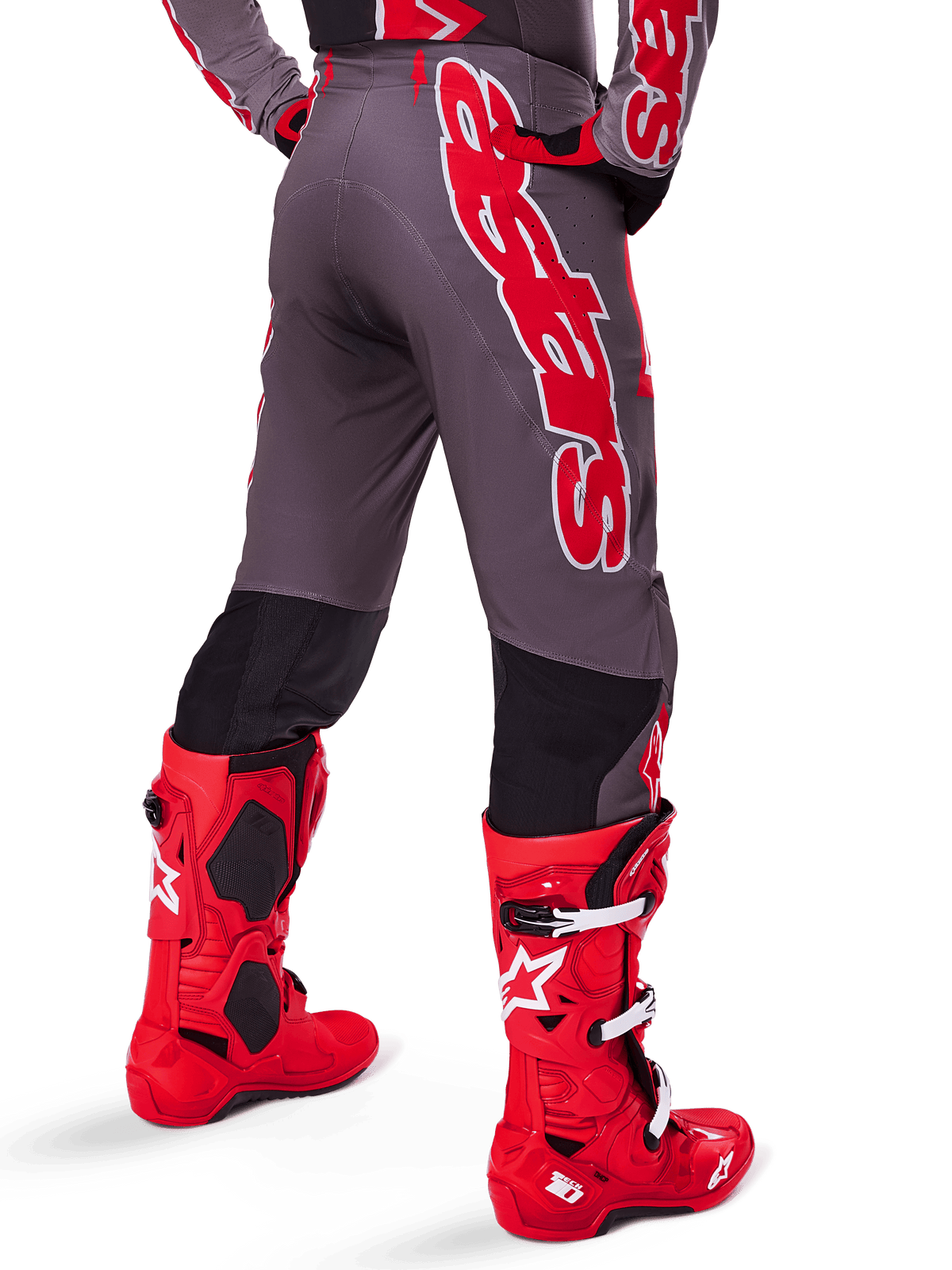 Alpinestars 2025 Supertech Lipan Gear Set, rear view of motocross rider, dark grey pants with large red vertical branding, matching red and grey jersey, bright red motocross boots, high-performance off-road racing gear