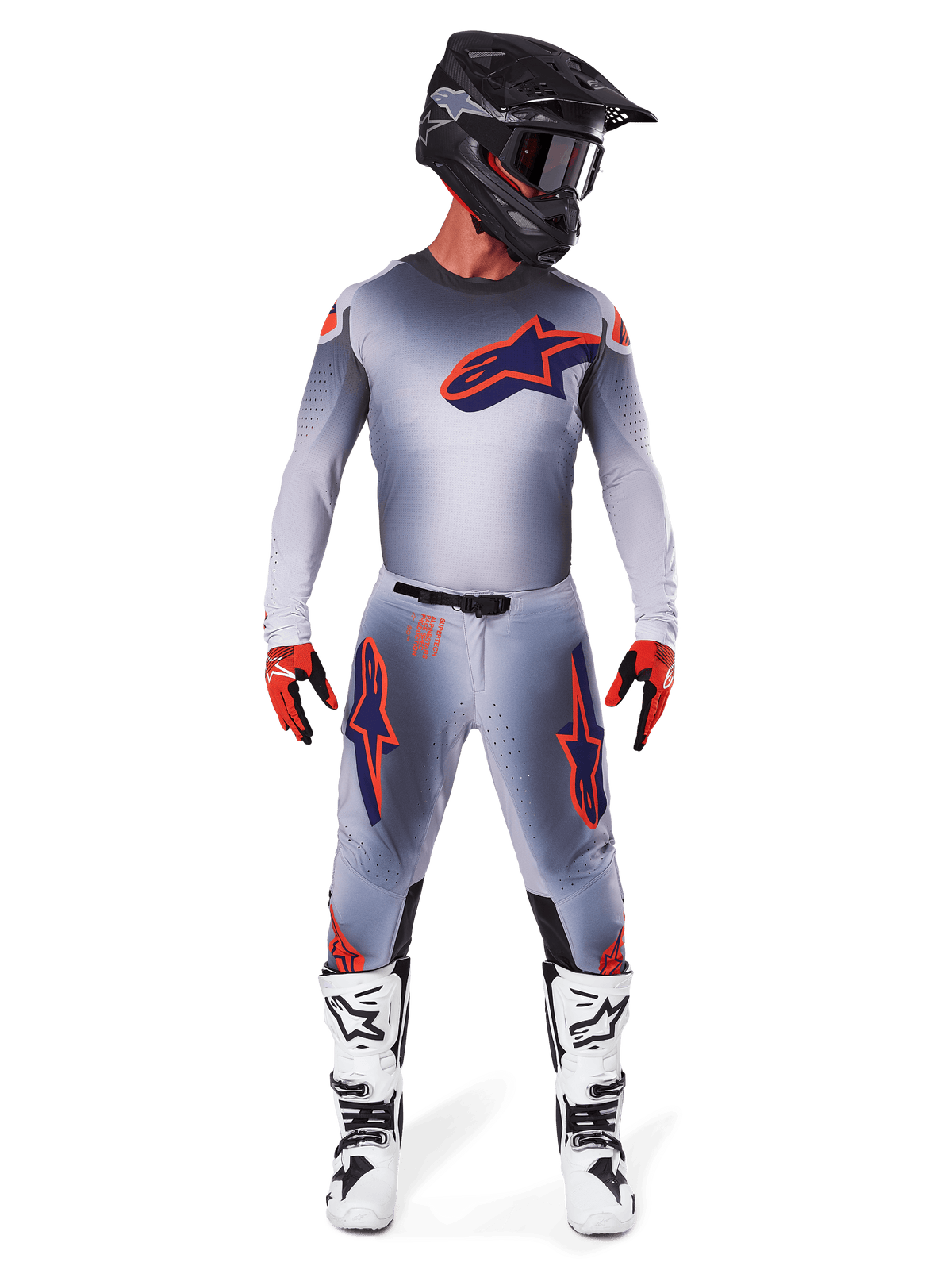 Motocross-kører iført Alpinestars 2025 Supertech Lipan bukser og matchende trøje i Grå Orange Fluo, med markante orange og navyblå logoer, kombineret med sort hjelm, røde handsker og hvide og sorte støvler, komplet racersæt til terrænkørsel.