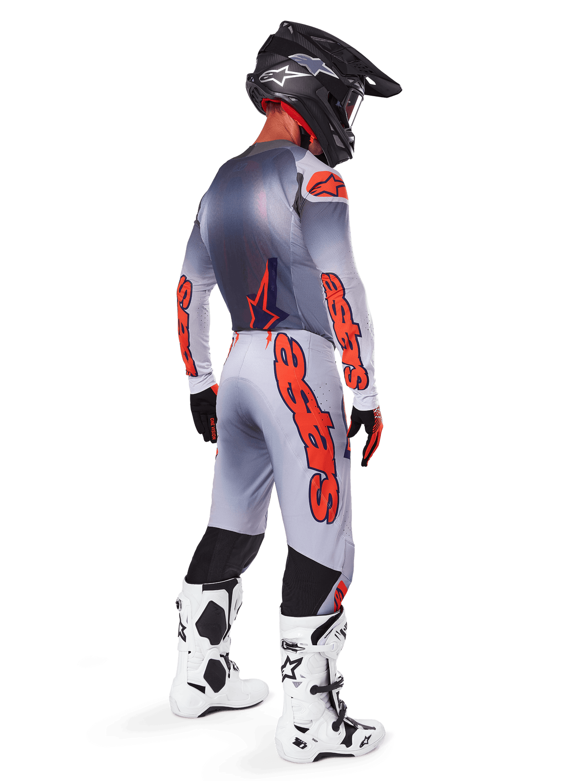 Motocrossrytter set bagfra iført Alpinestars 2025 Supertech Lipan-bukser i grå og fluoriserende orange, matchende langærmet trøje, sort hjelm og hvid-sorte tekniske støvler, komplet professionelt terrænracerudstyr.