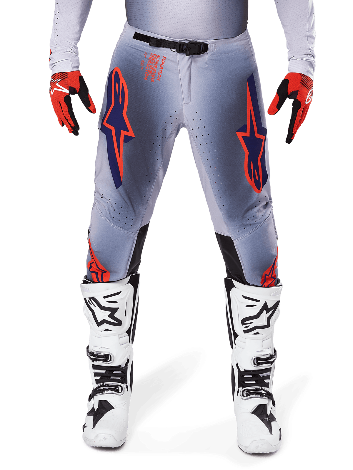 Alpinestars 2025 Supertech Lipan bukser, motocrossbukser, grå og orange fluo, bæres med røde og sorte handsker og hvide og sorte støvler, med store Alpinestars-stjernelogoer på lårene og ventilationsperforeringer til kørsel på professionelt niveau.