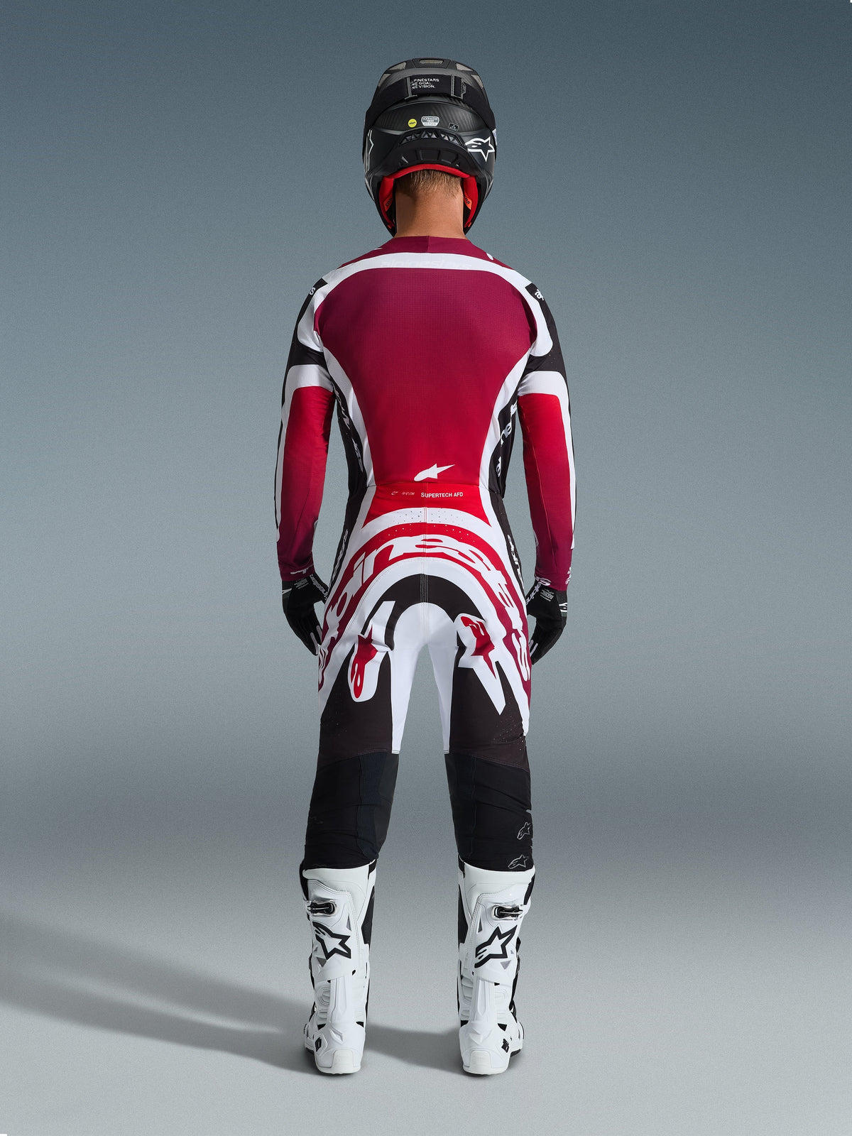 Motocross rider from behind wearing Alpinestars 2026 Supertech AFD Vista Pants, Black Red White, paired with a matching jersey, white racing boots, and black helmet, complete professional gear set for off-road racing