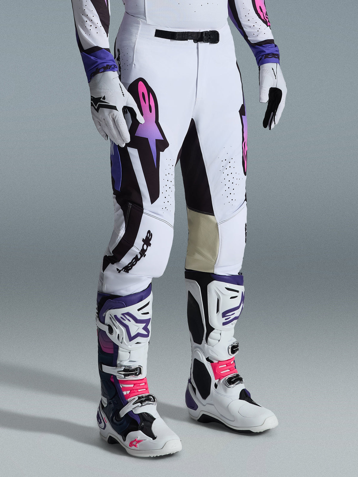 Alpinestars 2026 Supertech AFD Vista bukser, motocross-bukser, hvid, lilla og sort, med et lyserødt og lilla gradient Astar-logo, båret med matchende hvide og lilla motocross-støvler og -handsker, atletisk race-pasform med indvendige knæpaneler i lyst læder og perforerede detaljer.