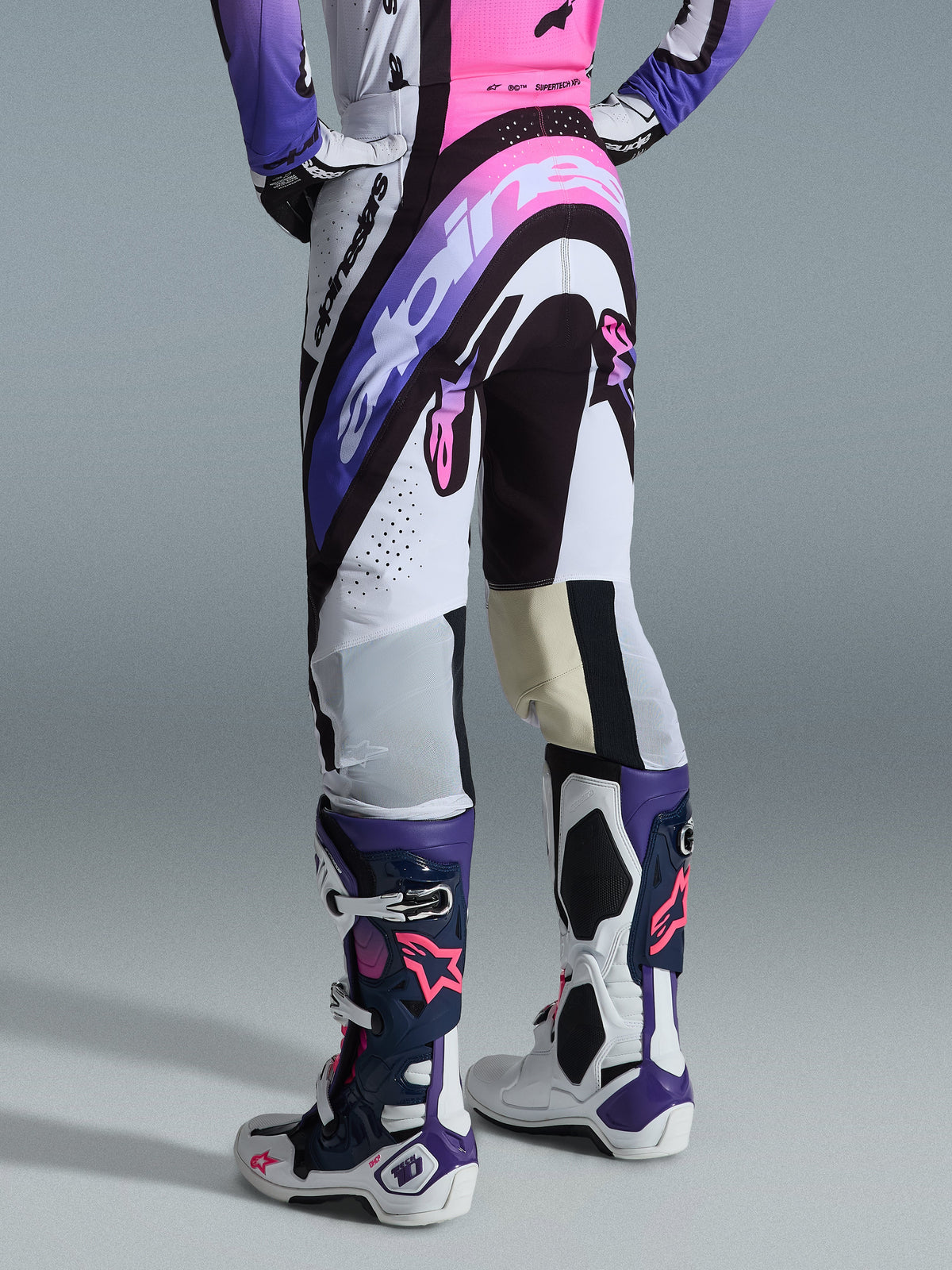 Alpinestars 2026 Supertech AFD Vista bukser, motocross-bukser, hvid, lilla og sort med lyserøde accenter, set bagfra båret med matchende trøje og Tech 10-støvler, med markant logografik og performance-materialer til elite terrænkørsel.