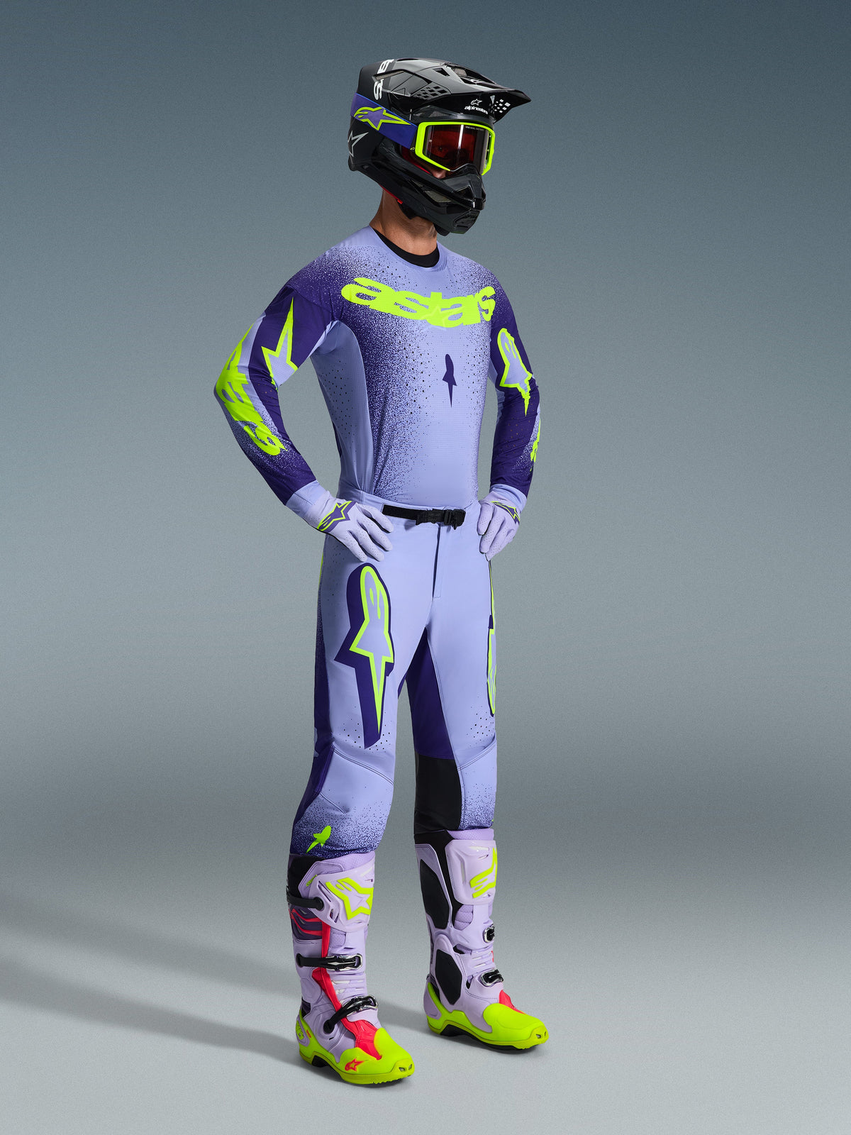 Alpinestars 2026 Supertech Scenz Pants, Motocross Pants, Purple and Yellow Fluo, worn by a rider in a complete racing outfit with a matching gradient jersey, lilac gloves, and coordinated yellow and purple boots, featuring a black helmet and goggles.