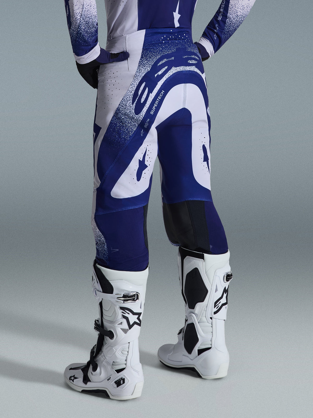 Alpinestars 2026 Supertech Scenz-bukser, motocross-bukser, lysegrå og mørkeblå, set bagfra båret med matchende trøje og hvide støvler, markant blå grafik med spættede detaljer, atletisk pasform til off-road racing.
