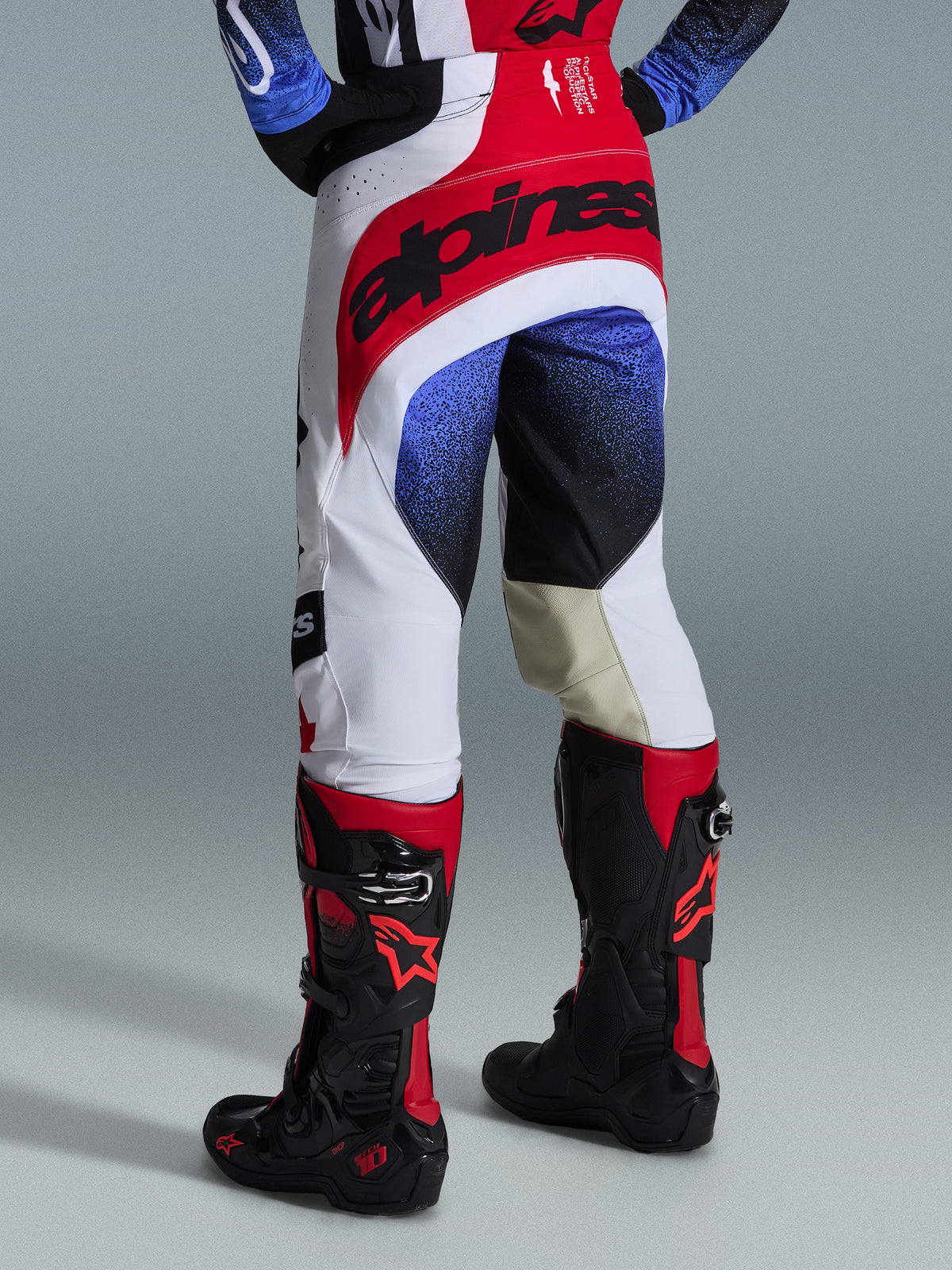 Alpinestars 2026 Techstar Knif bukser, motocross-bukser, hvid, rød og blå, set bagfra med rødt sædeparti og sort branding, blå og sorte nistrede mønstre på benene, båret med sorte og røde Tech 10-støvler, elite off-road racerudstyr