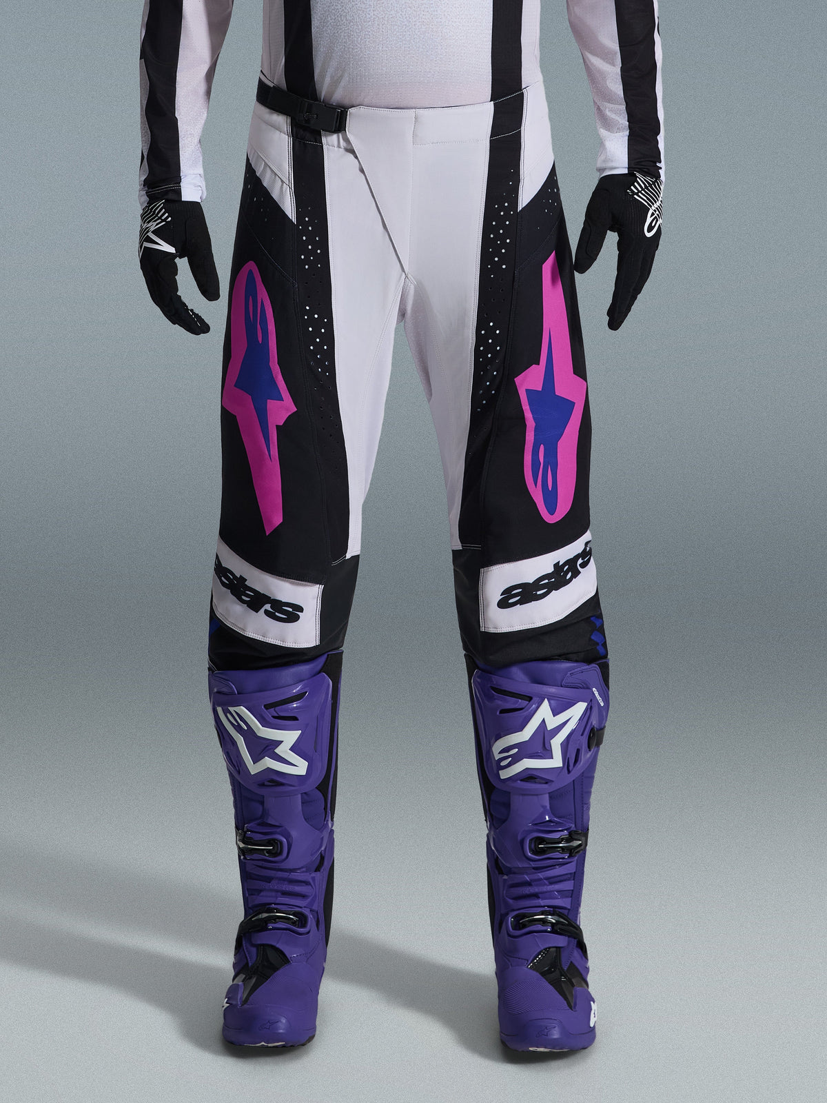 Alpinestars 2026 Techstar Knif bukser, motocross racingbukser, sort, hvid og lilla med pink og blå detaljer, båret med lilla racingstøvler og sorte handsker, med ergonomisk racingsnit og markant logografik til terrænkørsel