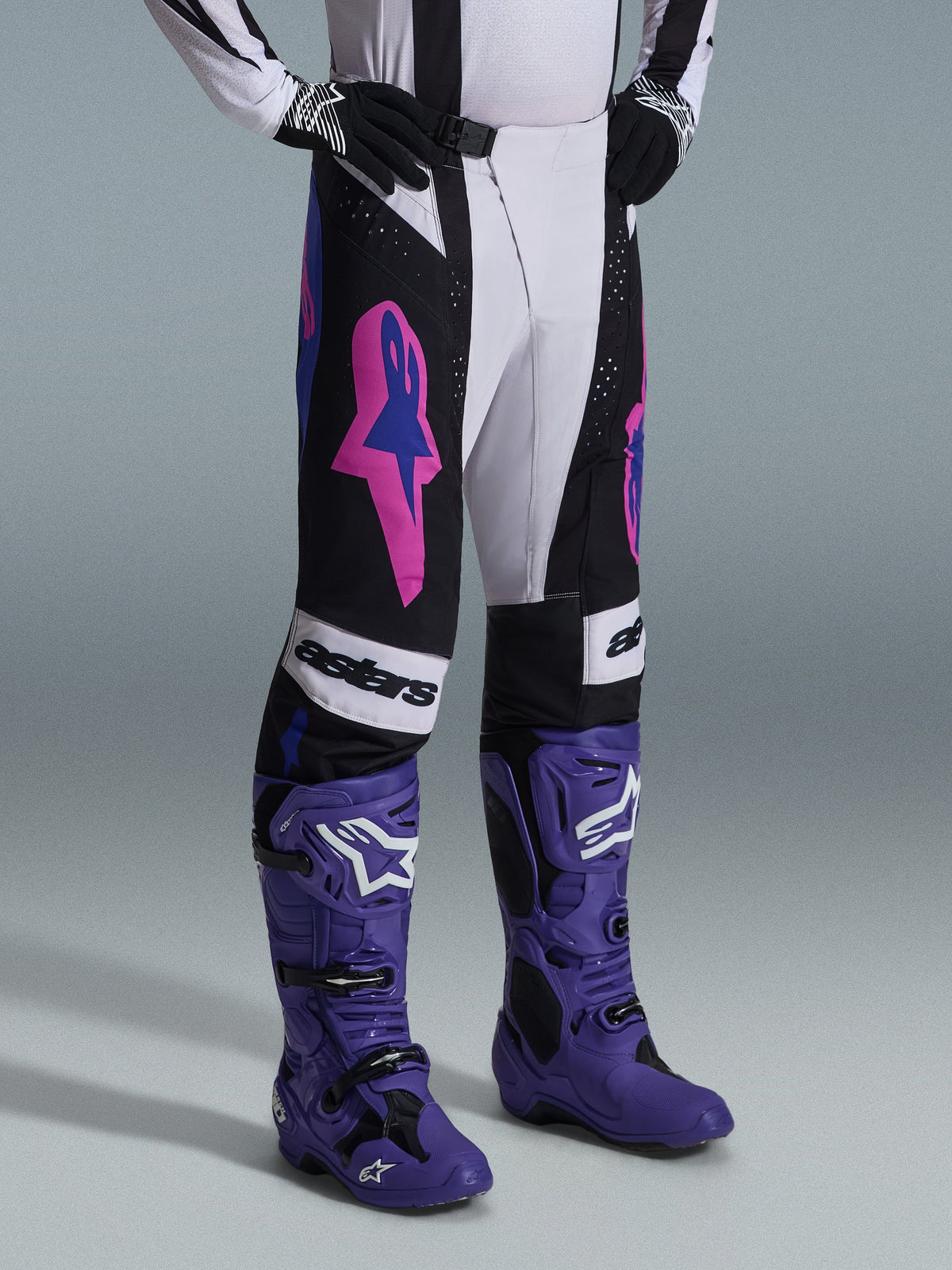 Alpinestars 2026 Techstar Knif bukser, sort, lysegrå og lilla, båret med matchende lilla motocrossstøvler, med markante lyserøde detaljer og 'astars' branding, professionelt motocross-racerudstyr