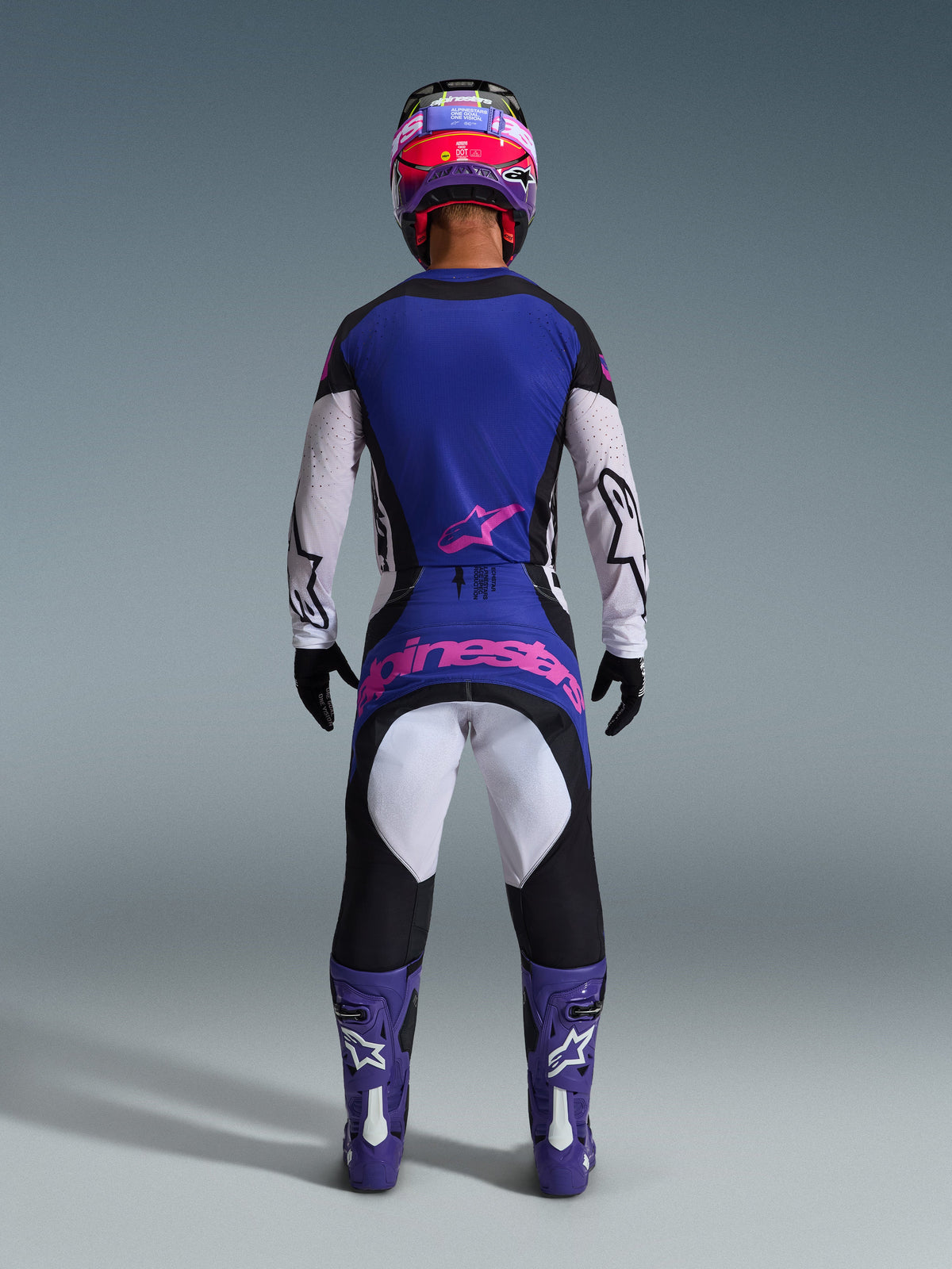 Alpinestars 2026 Techstar Knif-udstyrssæt, motocross-kører set bagfra, sort, lysegrå og lilla med lyserødt logo, båret med matchende lilla støvler og hjelm, professionelt racerudstyr til off-road kørsel