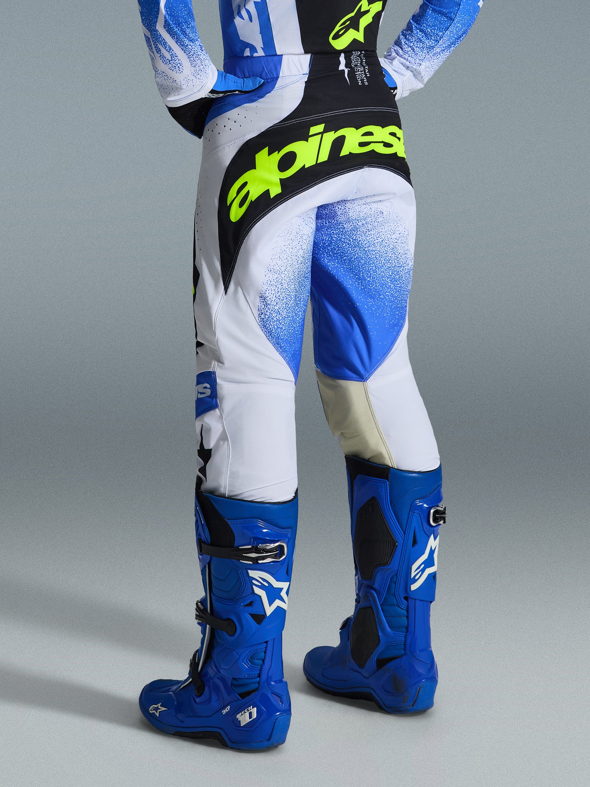 Alpinestars 2026 Techstar Knif bukser, motocrossbukser, Ucla Blue, sort og fluoriserende gul, set bagfra med hvide paneler og blåt gradient-spraymønster, markant logo i fluoriserende gul på det sorte sæde, båret med matchende blå Tech 10-støvler og trøje til off-road racing.