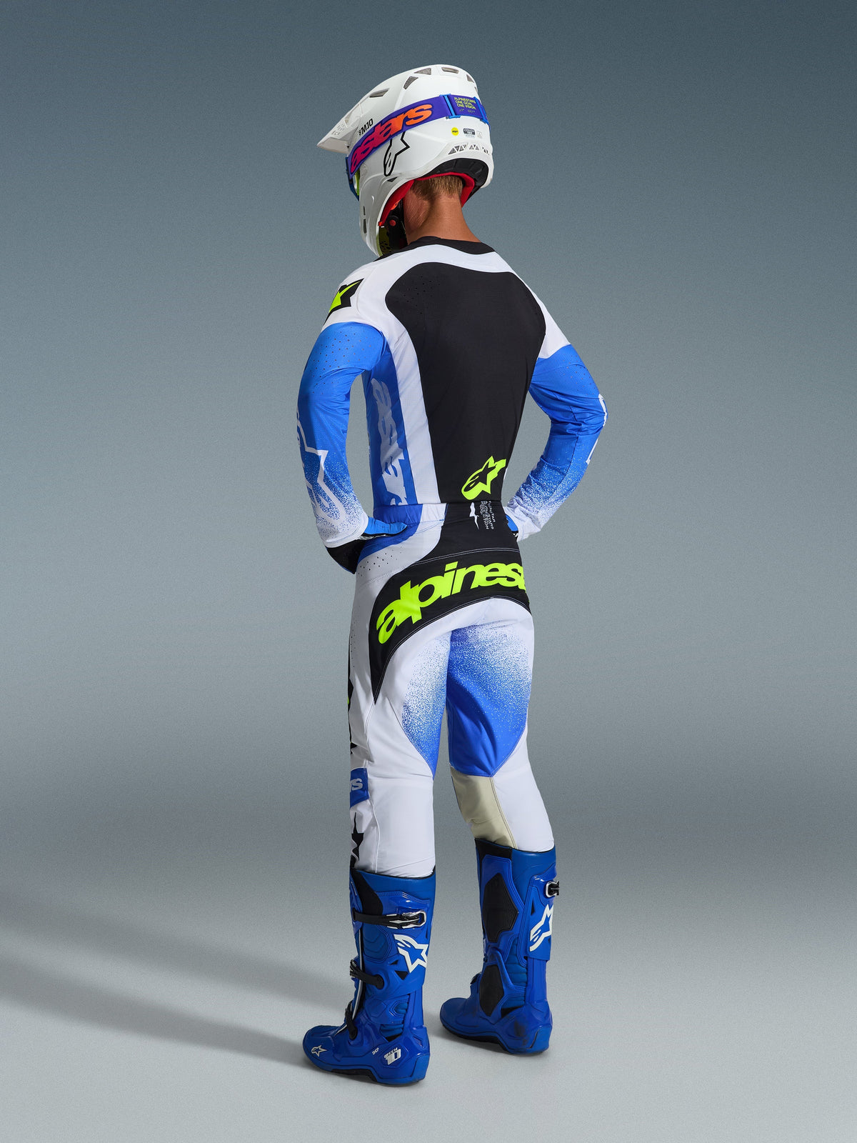 Alpinestars 2026 Techstar Knif-bukser, motocrossrytter set bagfra i Ucla Blue, sort og fluorescerende gul, med markant gul branding på sædet, koordineret trøje med blå ærmer, hvid hjelm og blå off-road-støvler.