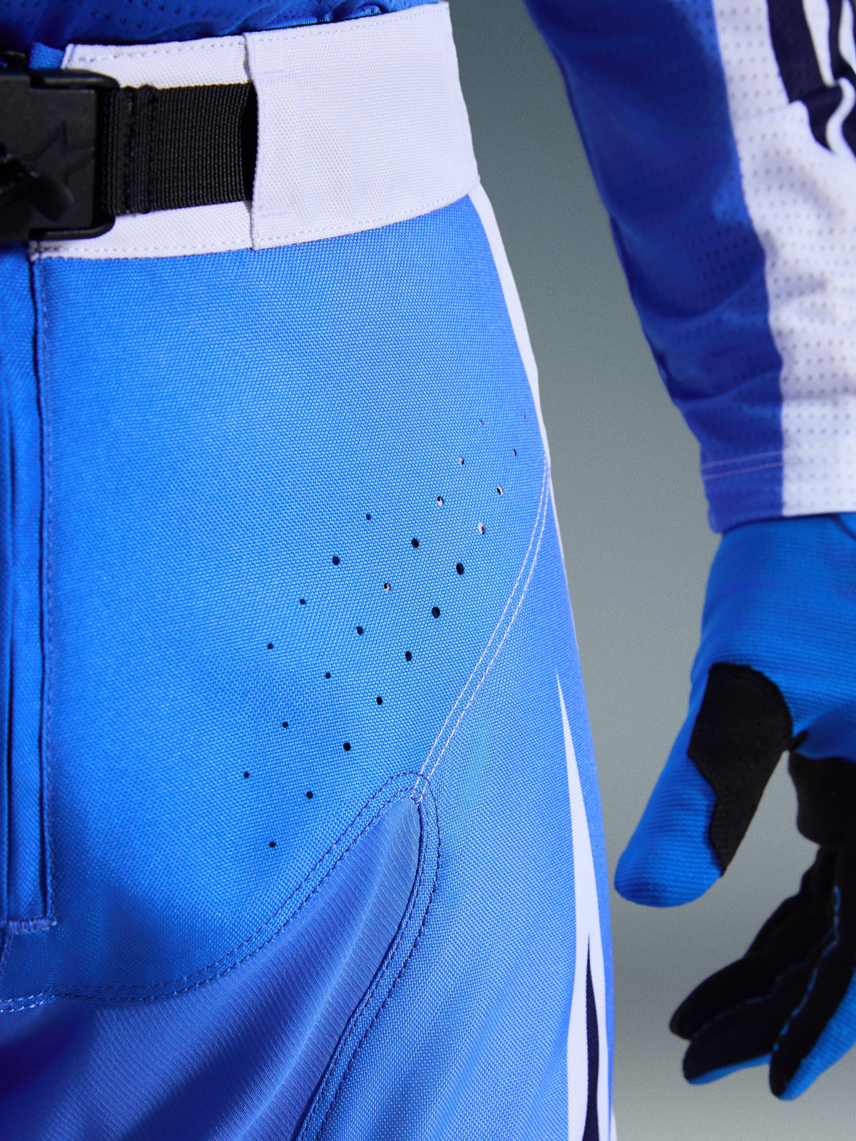 Alpinestars 2026 Techstar Knif bukser, motocrossbukser, Ucla blå og hvid, tærbillede af hofteområdet med laserperforeringer til ventilation, SX2 magnetisk spændelukning i taljen og matchende motocrosshandsker