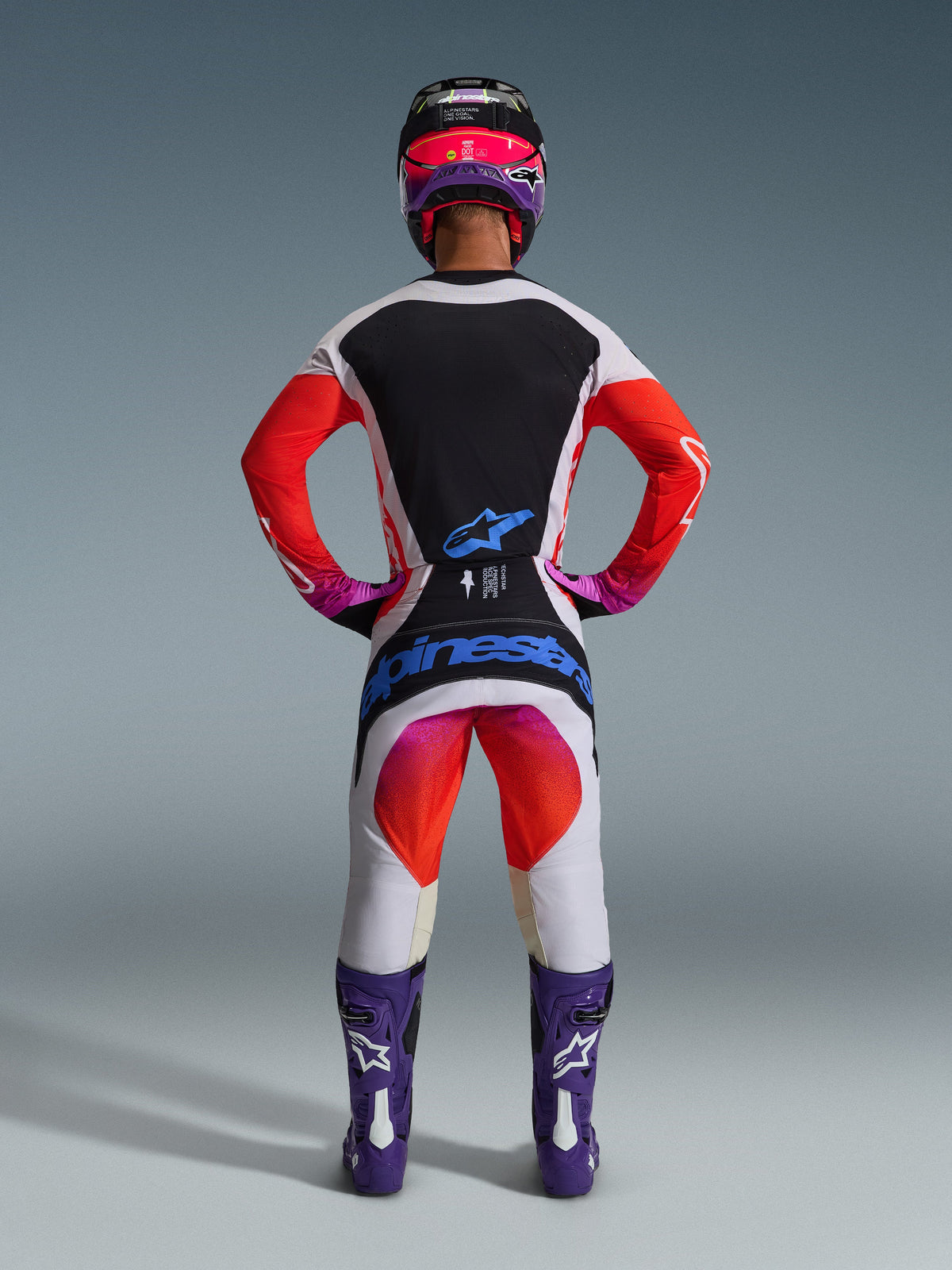 Alpinestars 2026 Techstar Knif-udstyrssæt, komplet motocross-udstyr set bagfra, hvid og sort trøje med røde gradient-ærmer, hvide bukser med røde og lyserøde detaljer, koordineret med lilla støvler og lyserød hjelm, markant blå branding, professionelt off-road racerudstyr