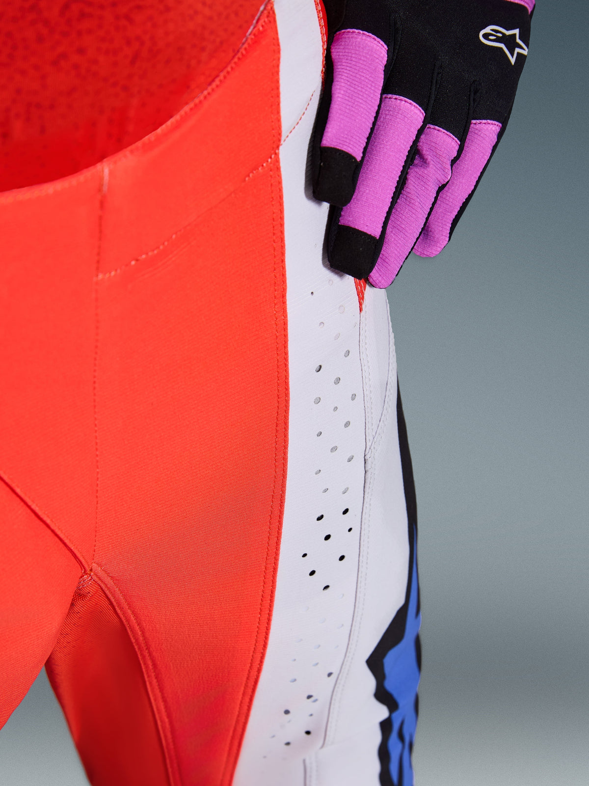 Alpinestars 2026 Techstar Knif bukser, motocross-bukser, neonorange og lysegrå med blå detaljer, nærbillede der viser laserskårne ventilationsperforeringer på låret, båret med en sort og lilla motocross-handske