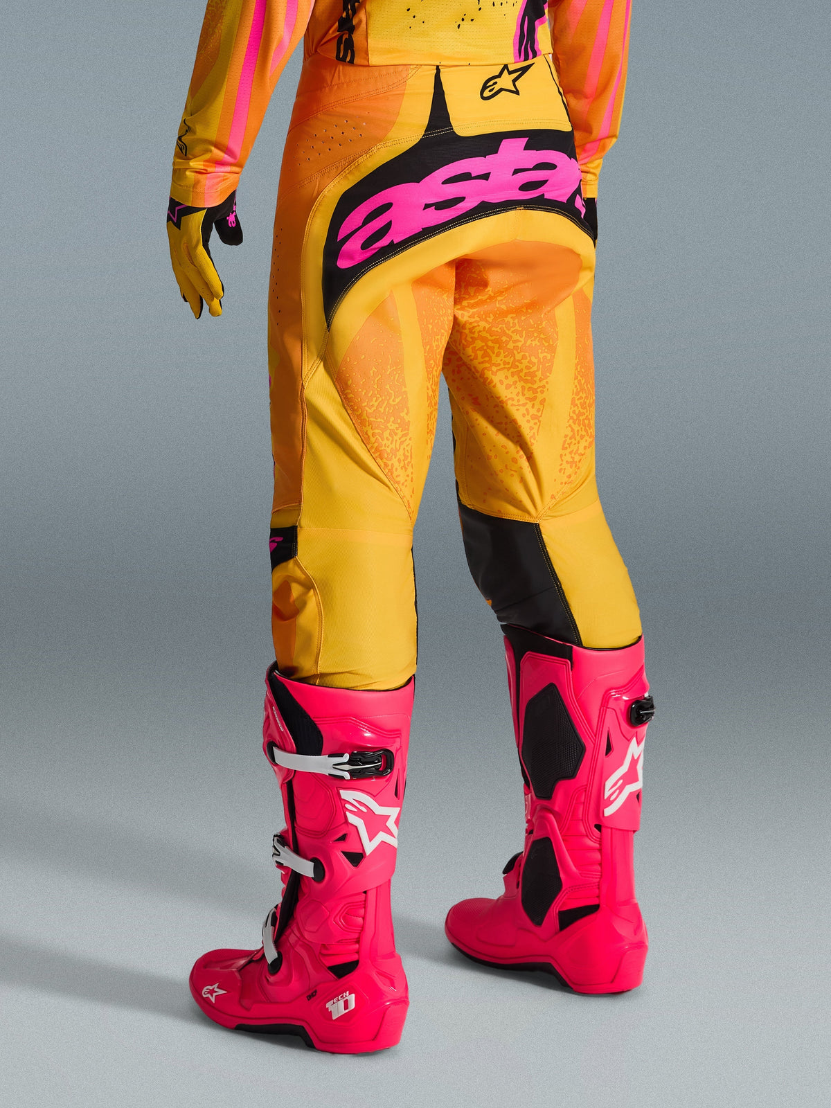 Alpinestars 2026 Techstar Nomur bukser, motocrossbukser, orange, gul og pink, set bagfra, med stor pink 'astars'-branding på sædet, kombineret med pink Tech 10-støvler og matchende trøje, professionelt racerudstyr til motocross
