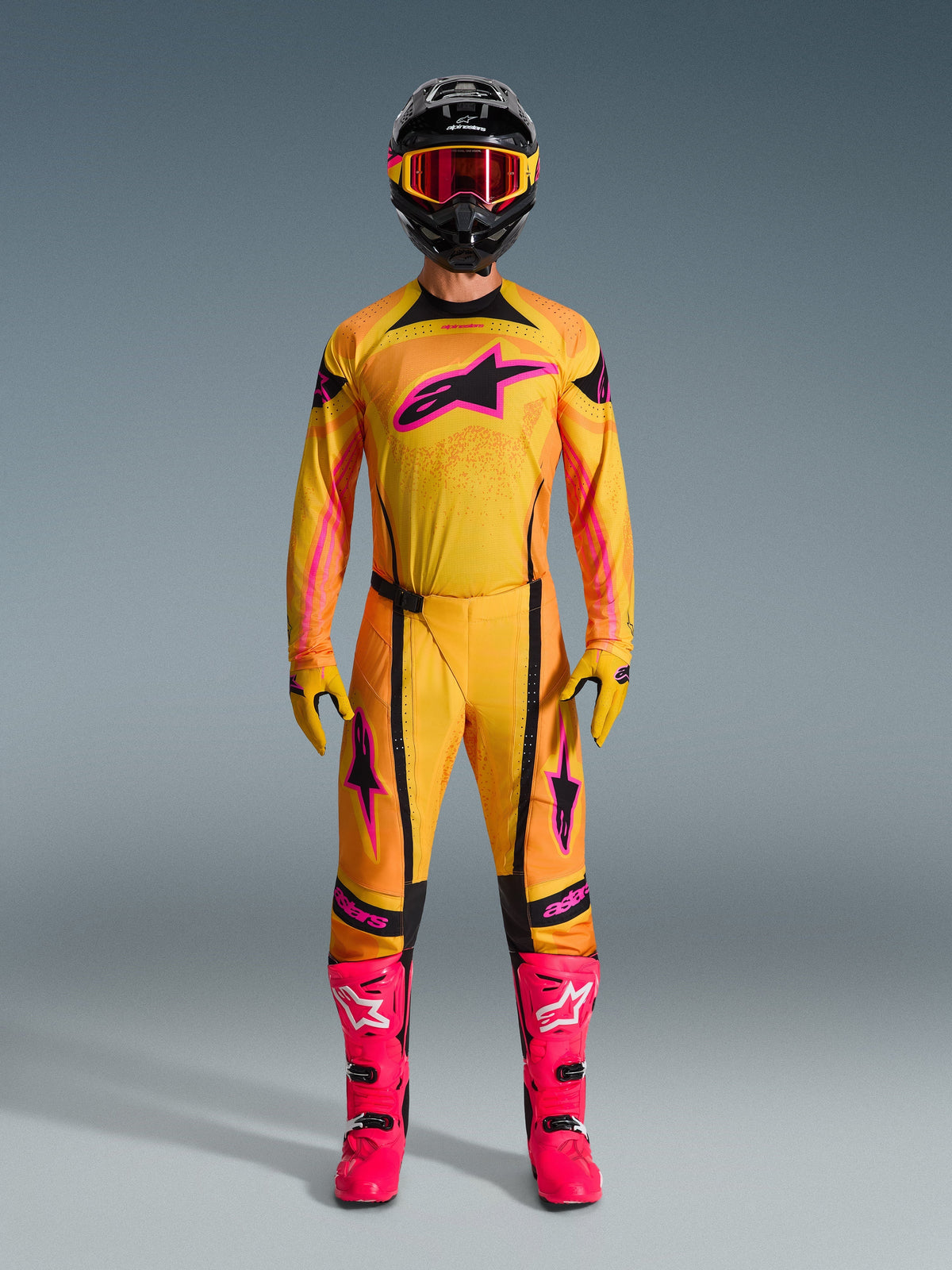 Alpinestars 2026 Techstar Nomur-udstyrssæt, motocrosskører iført komplet orange, gul og pink trøje og bukser, matchende gule og pink handsker, klare pink racingstøvler, sort hjelm med pink goggles, koordineret high-performance motocross-outfit.