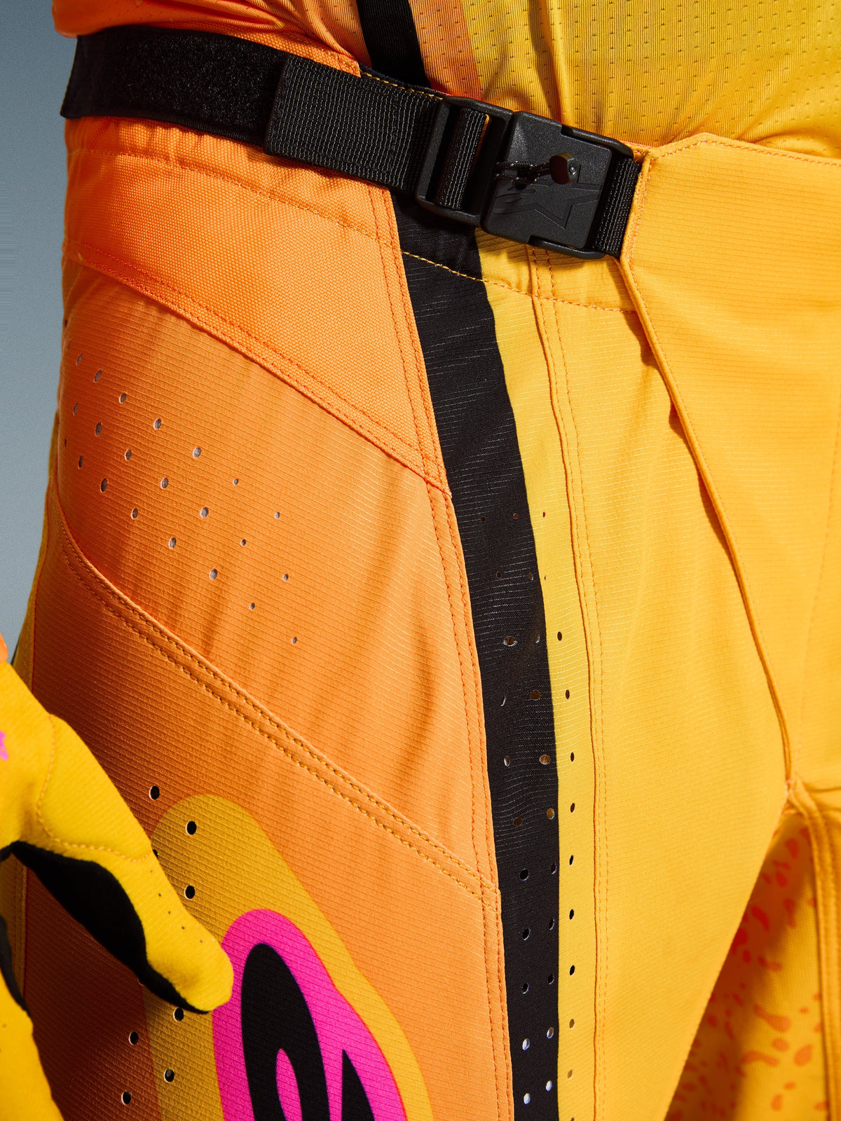 Alpinestars 2026 Techstar Nomur bukser, motocrossbukser, orange, gul og pink, nærbillede af taljeområdet med SX2 magnetisk spændelukning, sort justeringsrem og laserskårne ventilationsperforeringer på slidstærkt ripstop-materiale