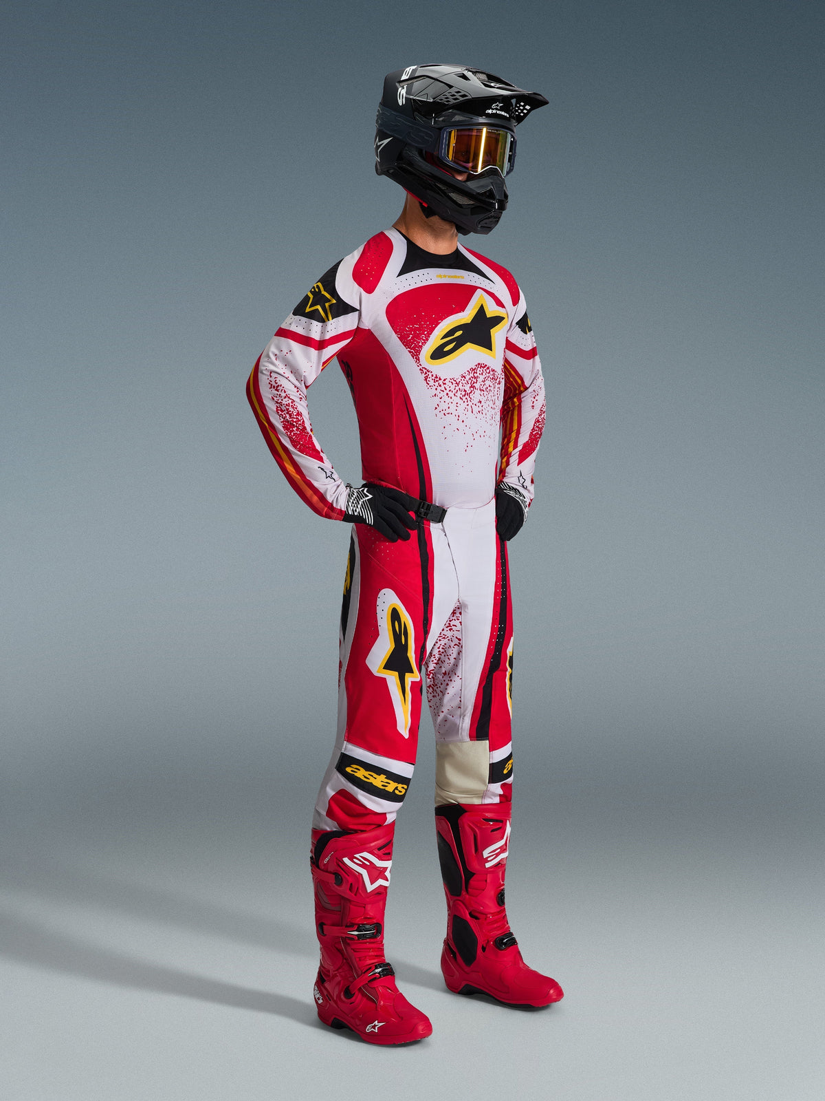 Motocrosskører iført komplet racerudstyr, 2026 Techstar Nomur trøje i rød, hvid og sort, matchende motocrossbukser med gule detaljer, sort hjelm med goggles, røde støvler og sorte handsker, koordineret outfit til off-road racing