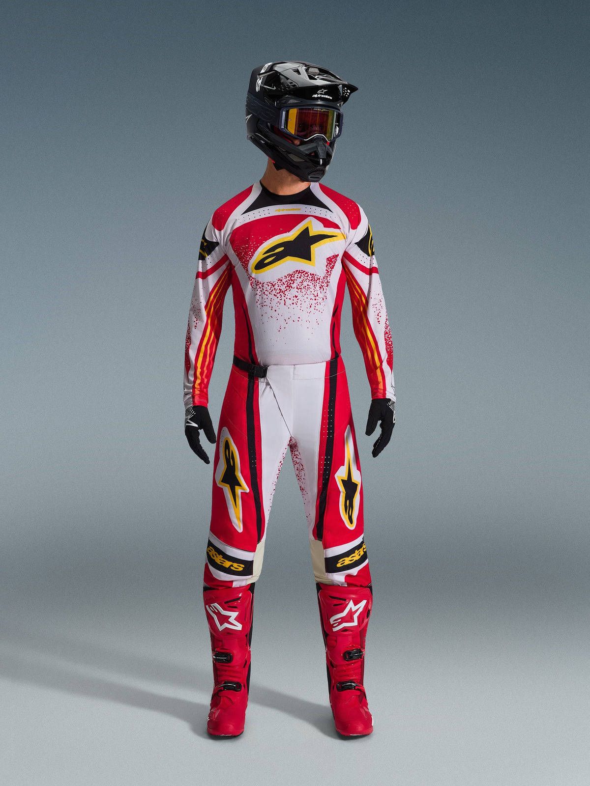 Alpinestars 2026 Techstar Nomur trøje, rød og hvid med sorte detaljer og gule logoer, båret af en motocrosskører med matchende bukser, røde støvler og en sort hjelm, professionelt off-road racerudstyr