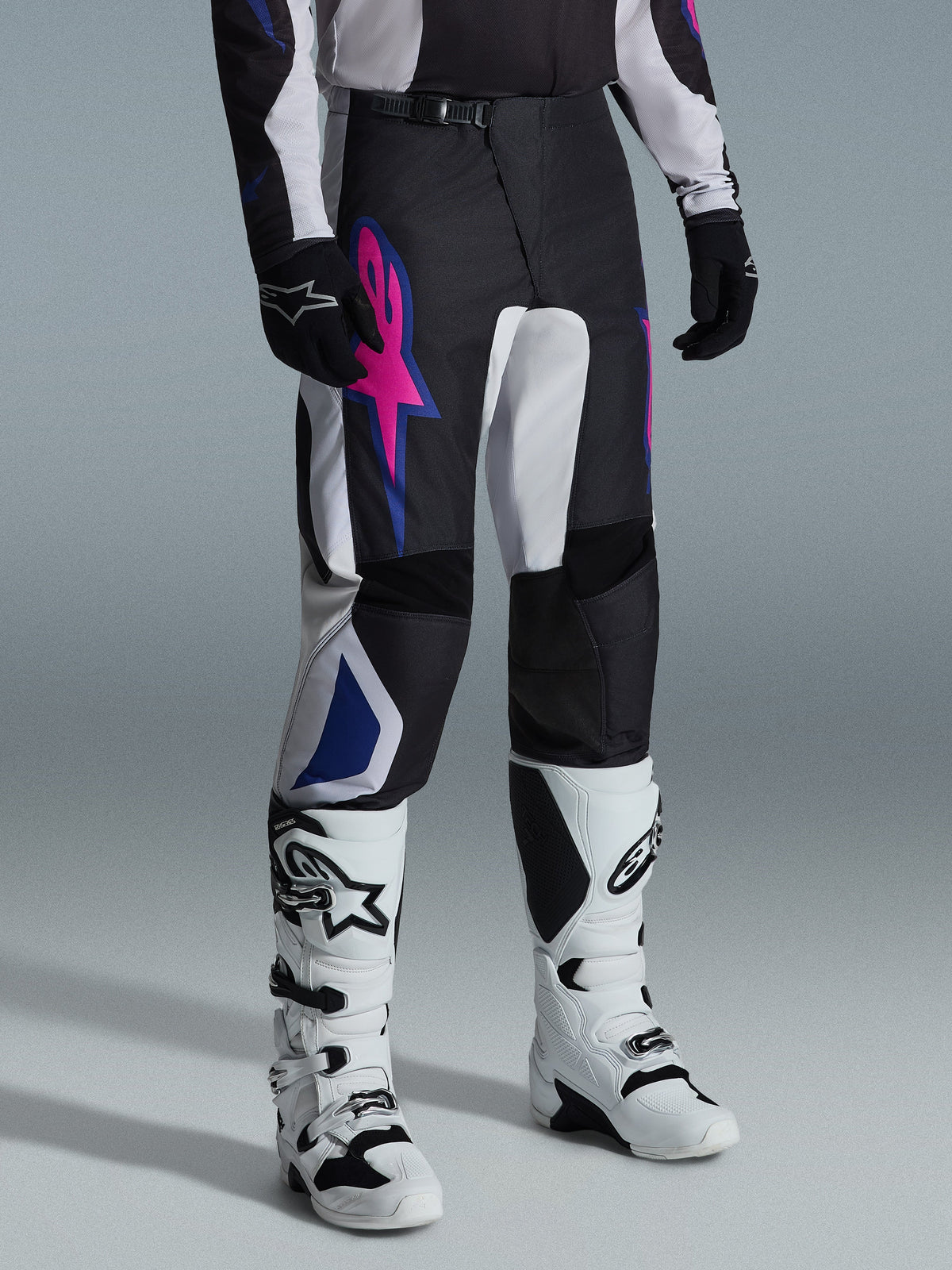 Alpinestars 2026 Fluid Grid bukser, motocross-bukser, sort, lysegrå og lilla, med et markant lyserødt stjernelogo og blå geometriske detaljer, båret sammen med hvide motocross-støvler og sorte handsker, ergonomisk off-road køreudstyr