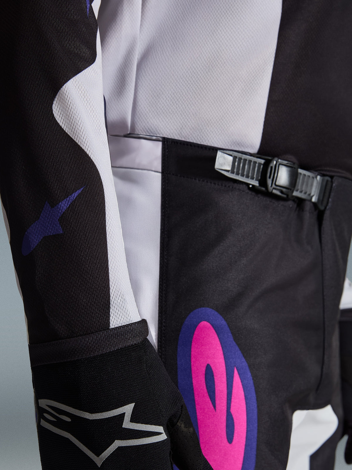Alpinestars 2026 Fluid Grid bukser, motocrossbukser, sort, lysegrå og lilla, nærbillede af skraldelukningen i taljen og en markant pink og lilla grafik på hoften, båret med en matchende trøje og sort handske.