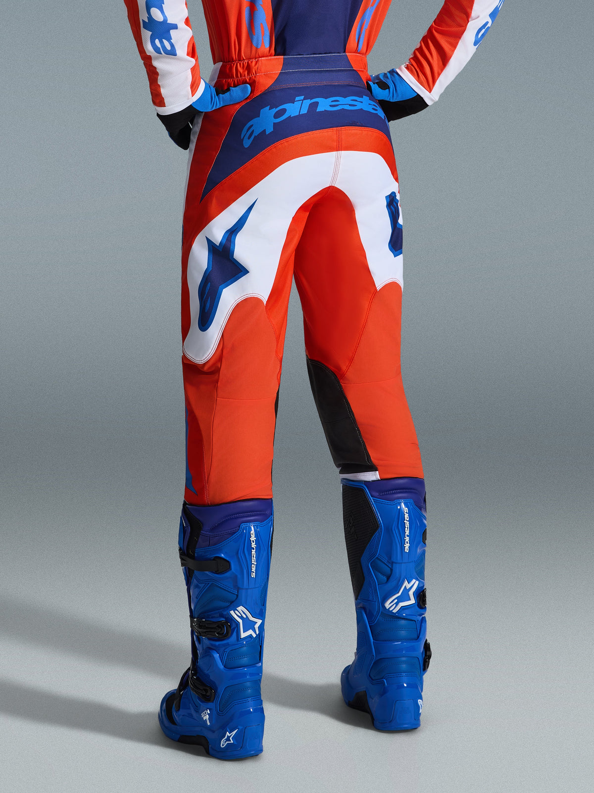 Alpinestars 2026 Fluid Grid bukser, motocross-bukser, orange og UCLA-blå med hvide paneler, set bagfra med tydeligt blåt logo på sædet og stjernelogo, kombineret med matchende blå motocross-støvler, professionelt udstyr til off-road kørsel