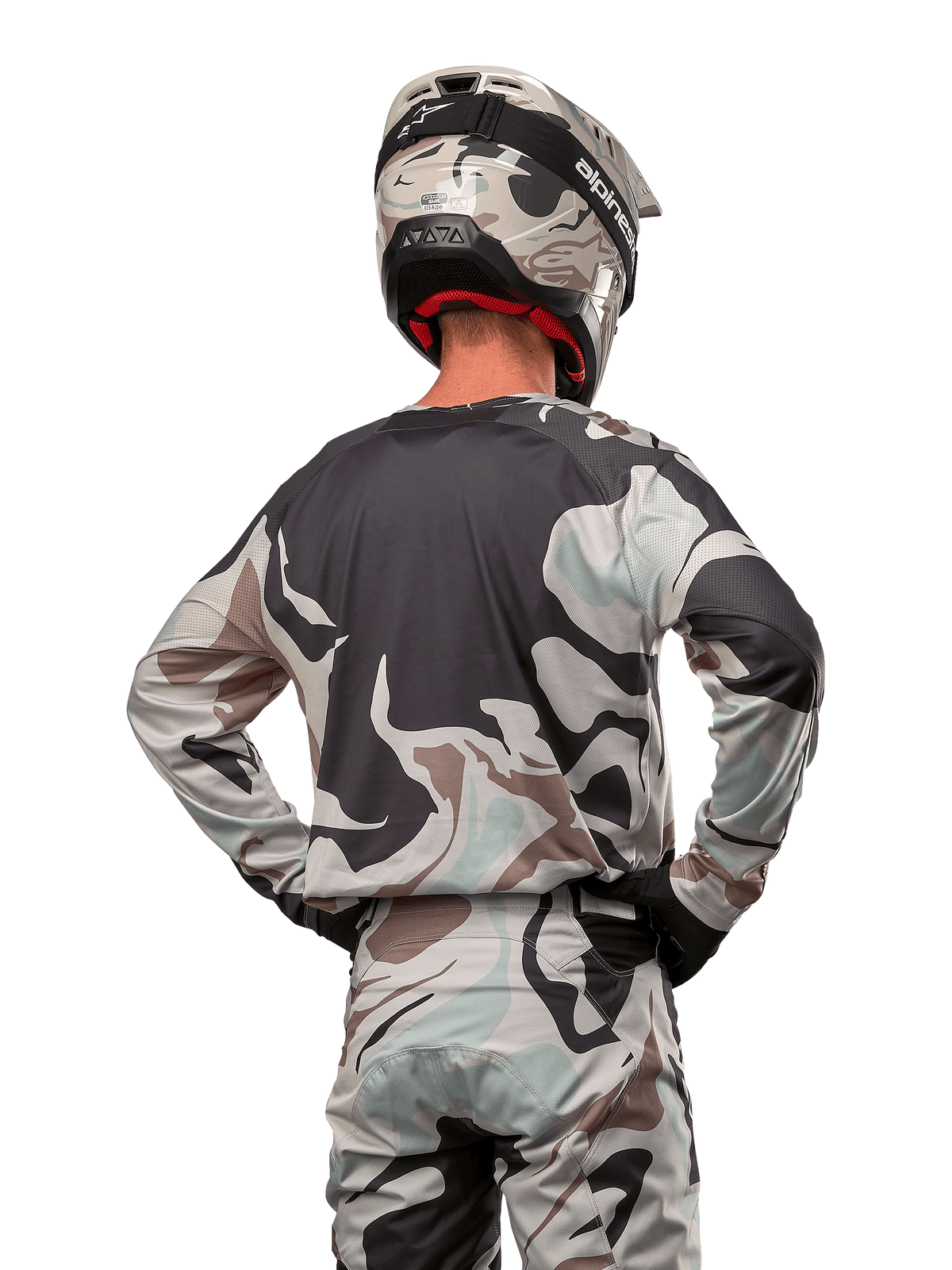 Motocross rider seen from behind wearing the Alpinestars 2024 Racer Tactical Jersey in Iron Camo Dust Gray, matching camouflage pants and helmet, hands on hips, coordinated off-road racing gear.