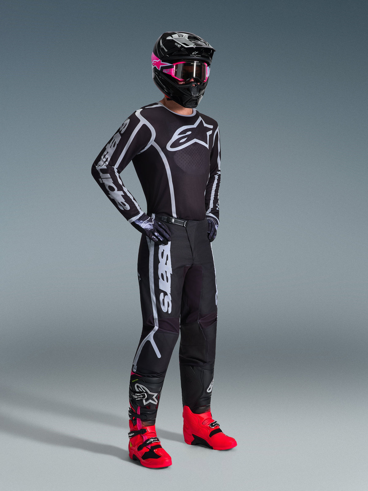 Alpinestars 2026 Fluid Apex bukser, motocrossbukser, sort og grå, båret med matchende sort og hvid jersey, sort hjelm med lyserøde goggles og skrigrøde støvler, med markant hvid branding på benene og et sport-fit design til off-road ræs