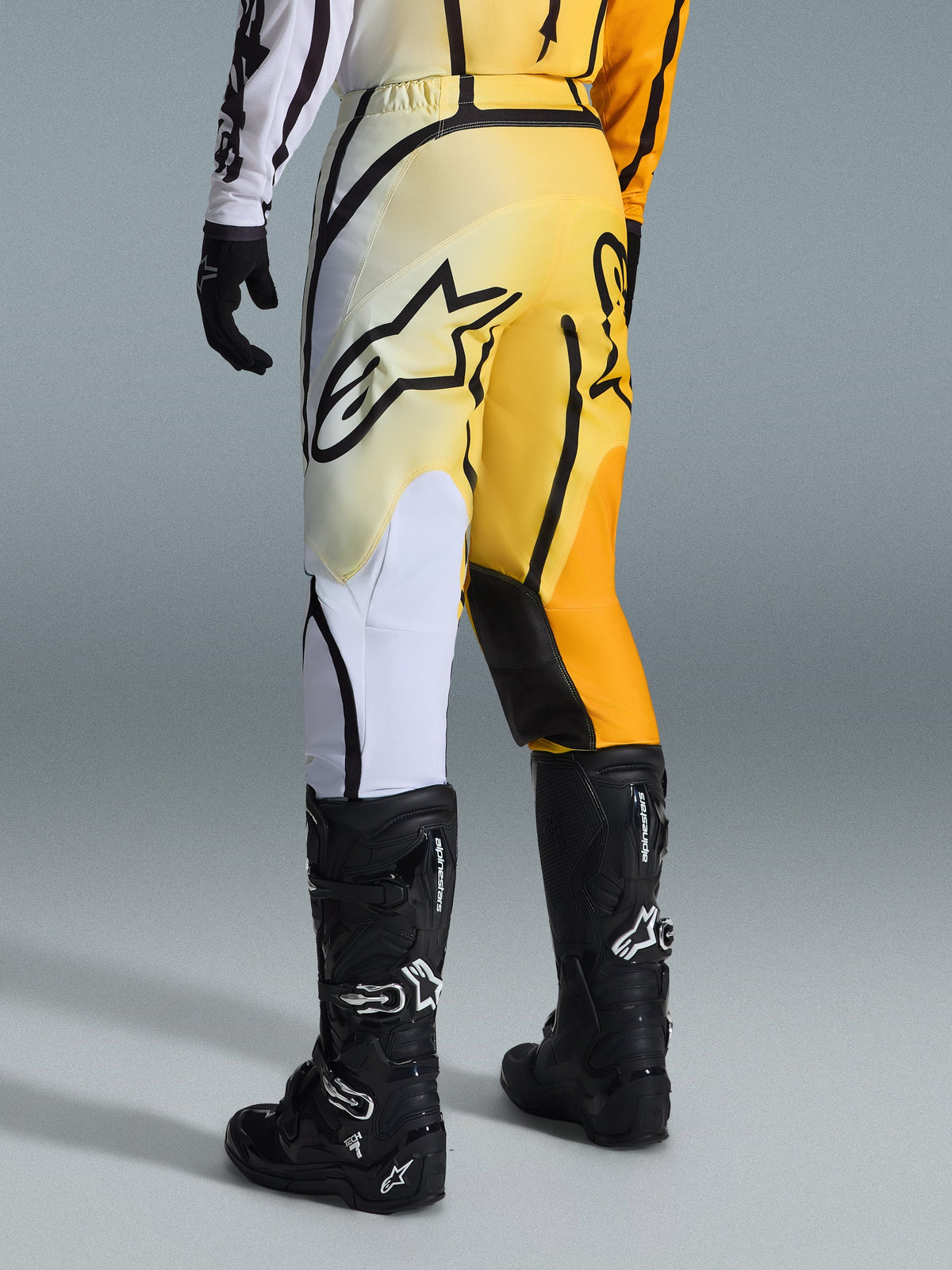 Alpinestars 2026 Fluid Apex bukser, motocrossbukser, gul og sort gradient med hvide og orange accenter, set bagfra, båret med matchende trøje og sorte Tech 7-støvler, med et markant sort Alpinestars-logo på sædet, performance-udstyr til terrænkørsel