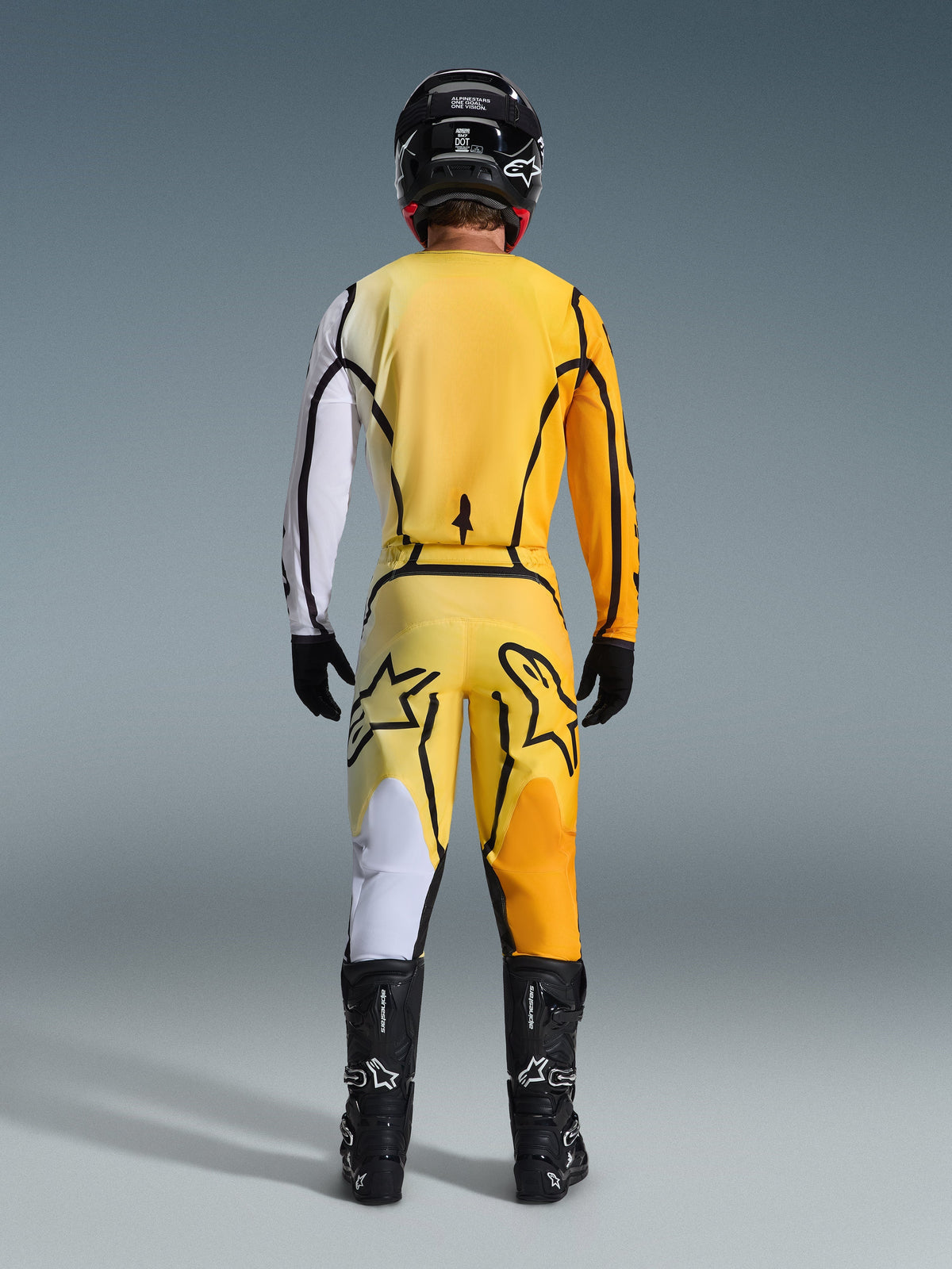 Alpinestars 2026 Fluid Apex bukser, motocrossbukser, gul og sort, set bagfra af en kører i fuldt motocross-udstyr, matchende trøje med hvide og orange gradueringer, sort hjelm, sorte støvler og sorte handsker, koordineret off-road outfit.
