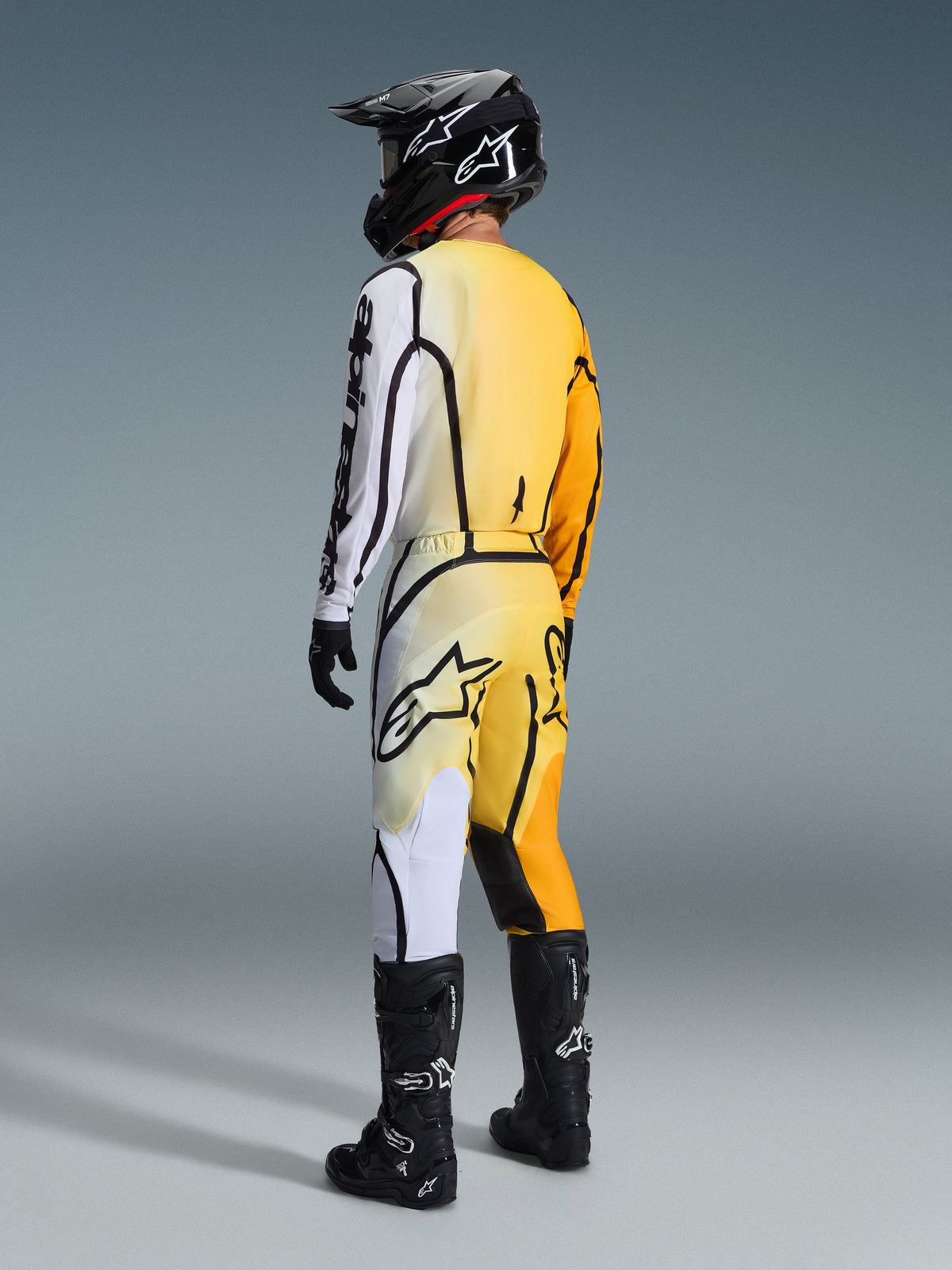 Alpinestars 2026 Fluid Apex bukser, motocrossbukser, gul og hvid graduering med sorte detaljer, set bagfra af kører i komplet racerudstyr inklusiv matchende jersey, sort hjelm og sorte støvler