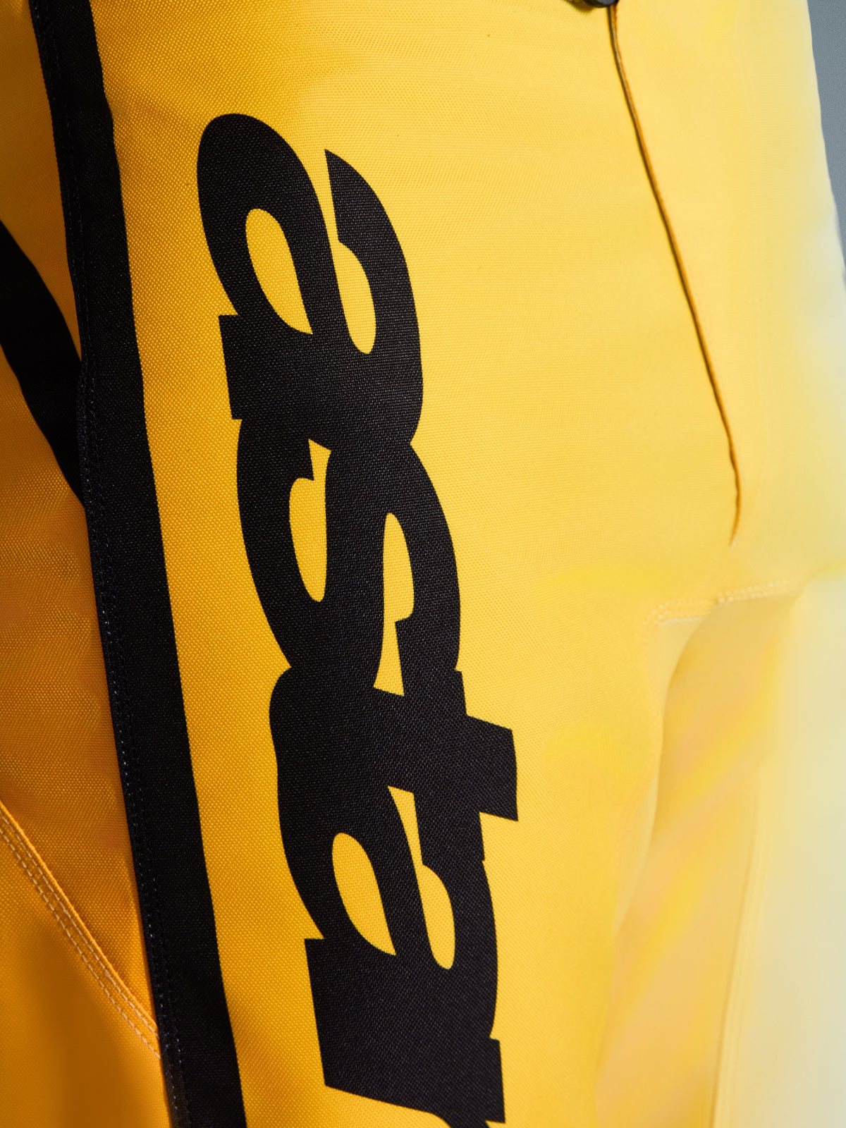 Nærbillede af Alpinestars 2026 Fluid Apex bukser, motocross-bukser, gul og sort, med et stort lodret sort logo, tekstureret holdbart materiale og ergonomiske detaljer til off-road-ydeevne