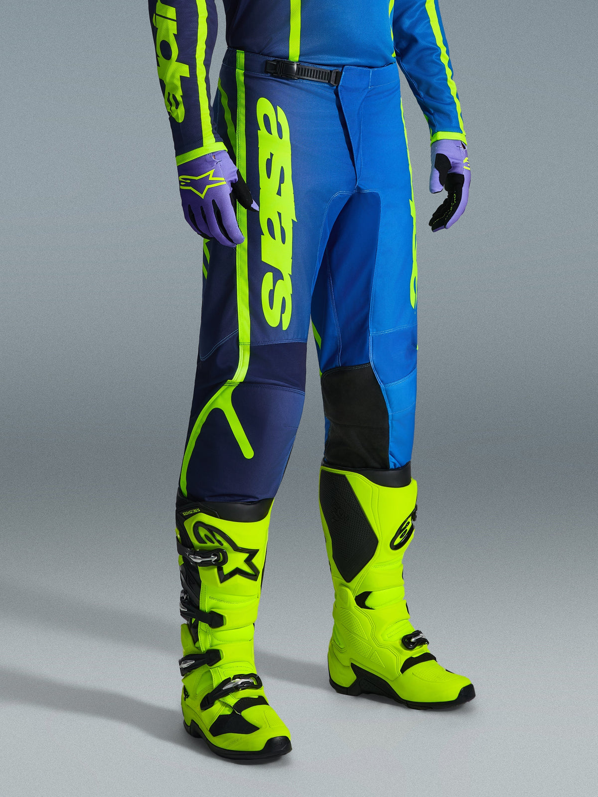 Alpinestars 2026 Fluid Apex bukser, motocrossbukser, blå og gul fluo, båret med matchende handsker og klare gul fluo-støvler, med markant lodret branding, forstærkede knæpaneler og en sikker skraldelukning i taljen.