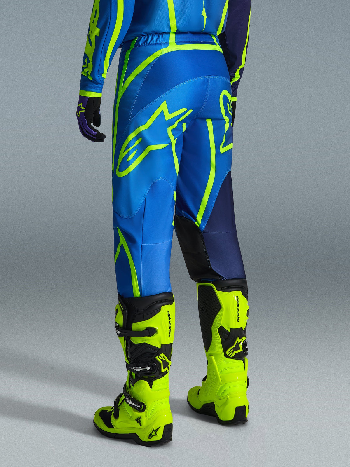 Alpinestars 2026 Fluid Apex bukser, motocrossbukser, blå og neongul, set bagfra af en kører i matchende udstyr og neongule støvler, med markante Alpinestars-logoer og ergonomisk design