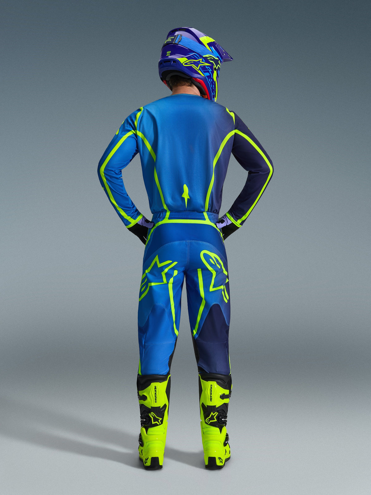 Alpinestars 2026 Fluid Apex bukser, motocrossbukser, blå og gul fluo, set bagfra af kører i komplet racerudstyr, matchende trøje og hjelm, neongule støvler, koordineret atletisk pasform til motocross