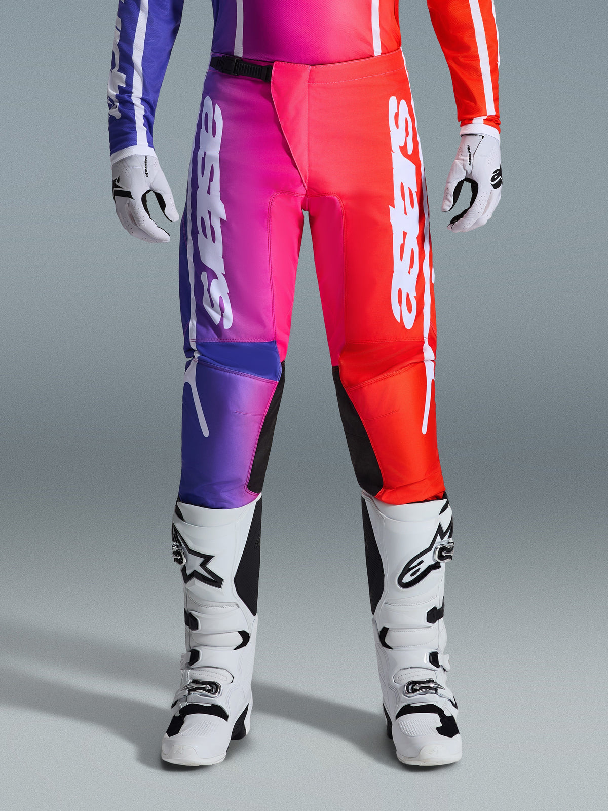 Alpinestars 2026 Fluid Apex bukser, motocrossbukser, flerfarvet lilla, lyserød og rød farveovergang, stort hvidt Alpinestars-branding på benene, kombineret med hvide og sorte motocross-støvler og -handsker, professionelt off-road racerudstyr