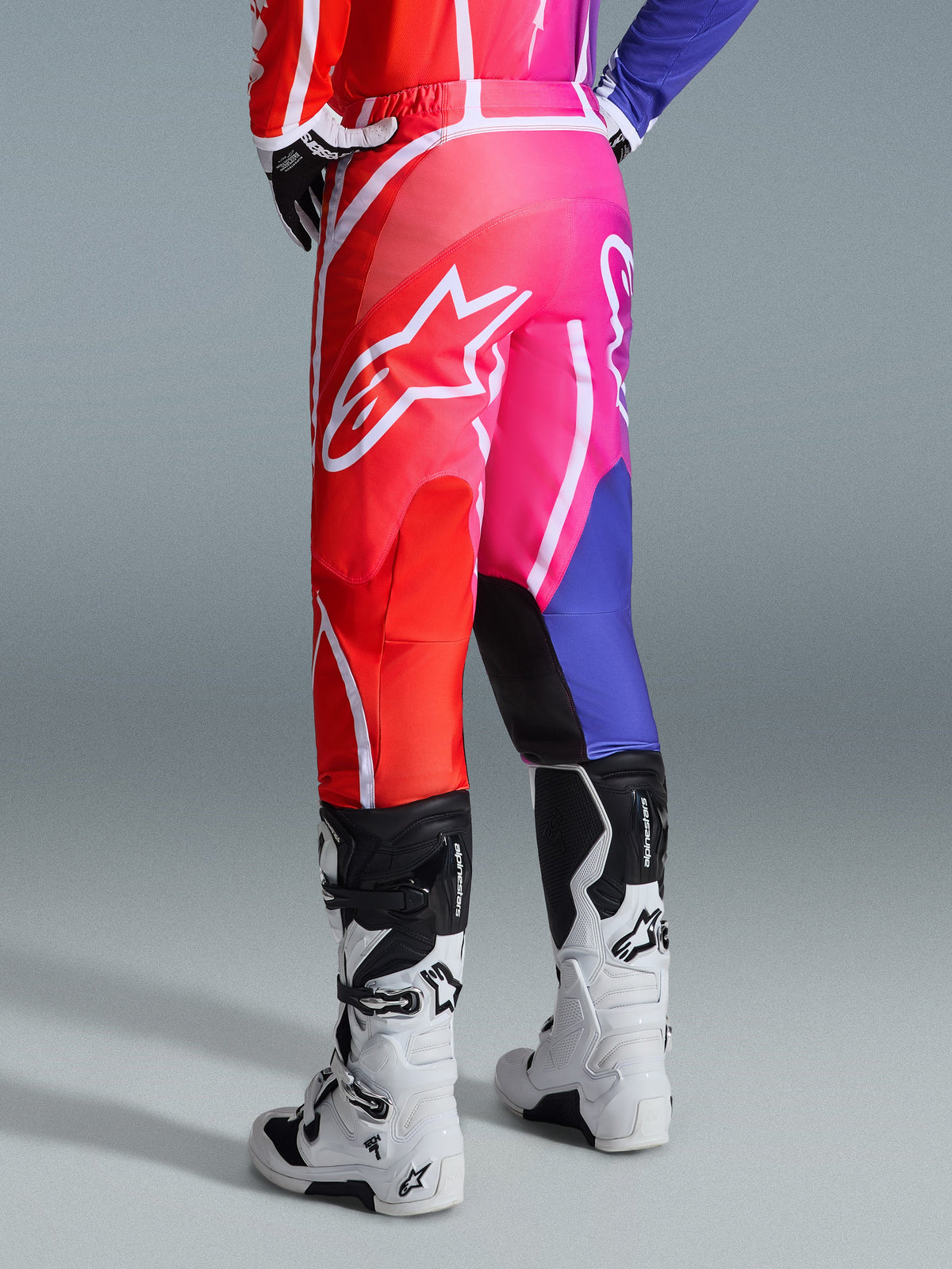Alpinestars 2026 Fluid Apex bukser, motocross-bukser, flerfarvet rød, pink og lilla, set bagfra af kører iført bukser med hvide og sorte motocross-støvler, stort hvidt Alpinestars-logo, levende gradientdesign