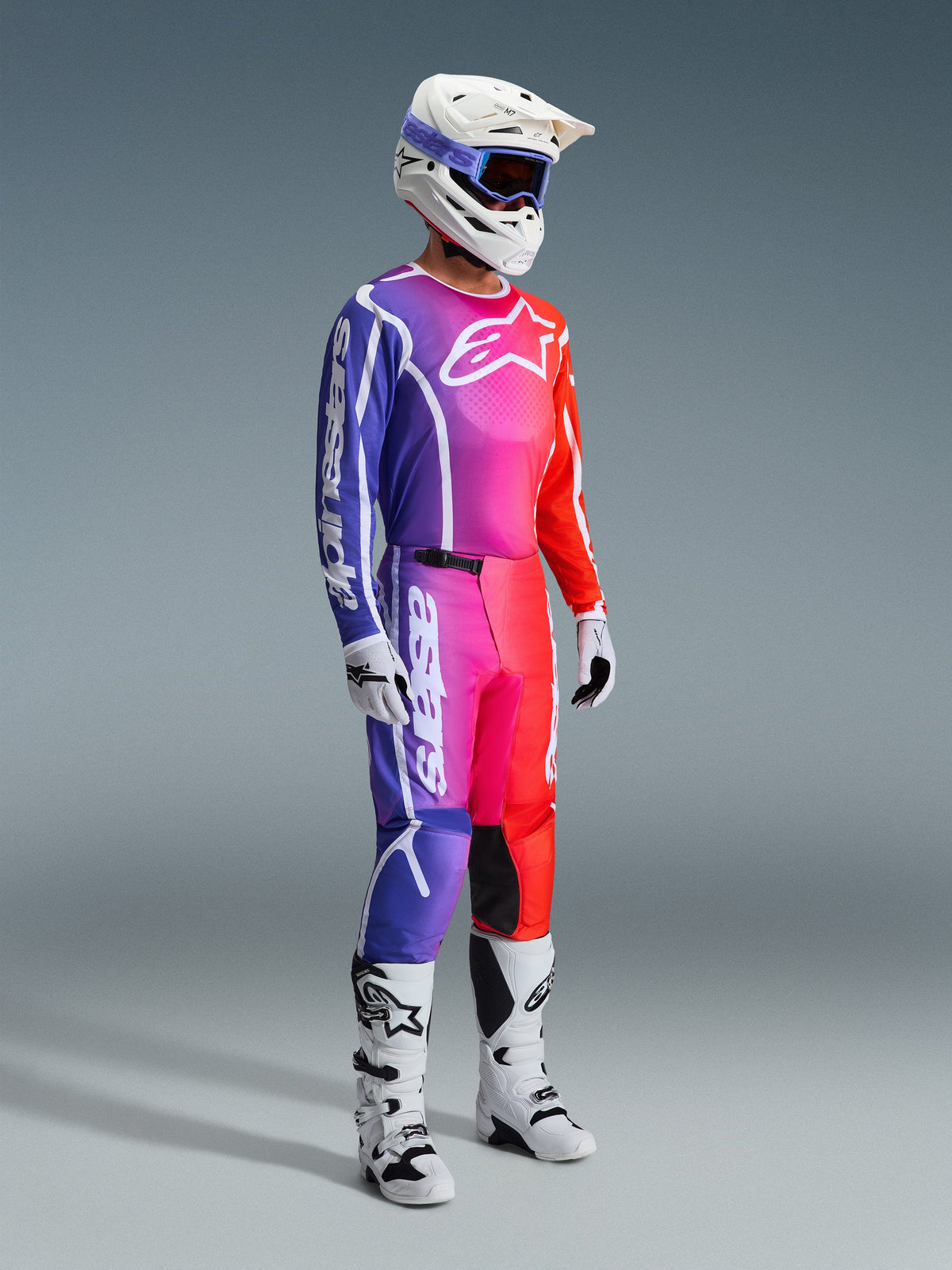 Alpinestars 2026 Fluid Apex bukser, motocrossbukser, flerfarvet graduering af lilla, pink og orange, bæres med matchende trøje, hvid hjelm og hvide støvler, markant hvid branding og ergonomisk design til off-road racing