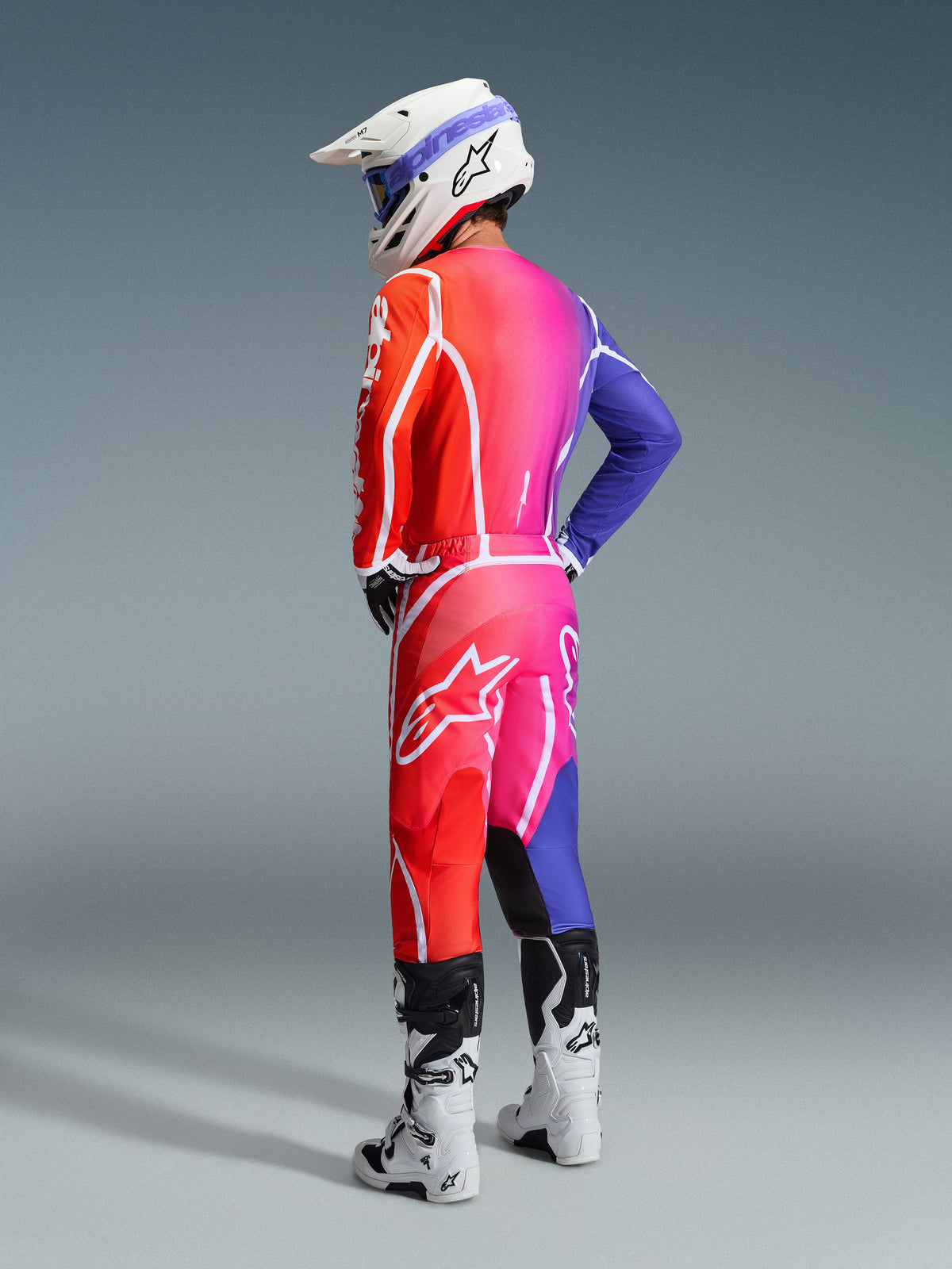 Alpinestars motocross-kører iført 2026 Fluid Apex-udstyr, flerfarvet jersey og bukser med en rød, pink og lilla gradient og hvide logoer, hvid hjelm og hvide støvler, koordineret sæt til off-road racing