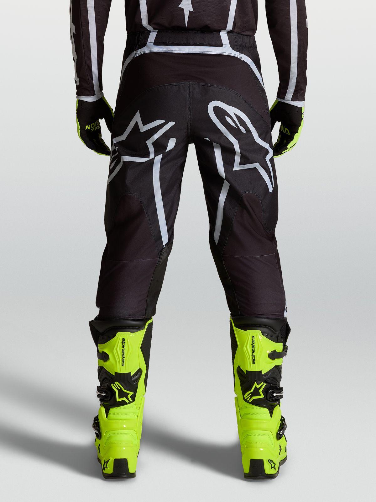 Alpinestars Fluid Apex V2 bukser, sort og sølv, herre motocrossbukser set bagfra med hvidt logo-grafik og gule støvler