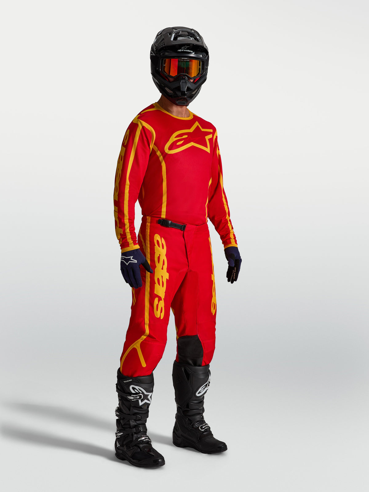 Alpinestars Fluid Apex V2 bukser, motocrossudstyr i rød og guld, vist på model med trøje og støvler til off-road kørsel.