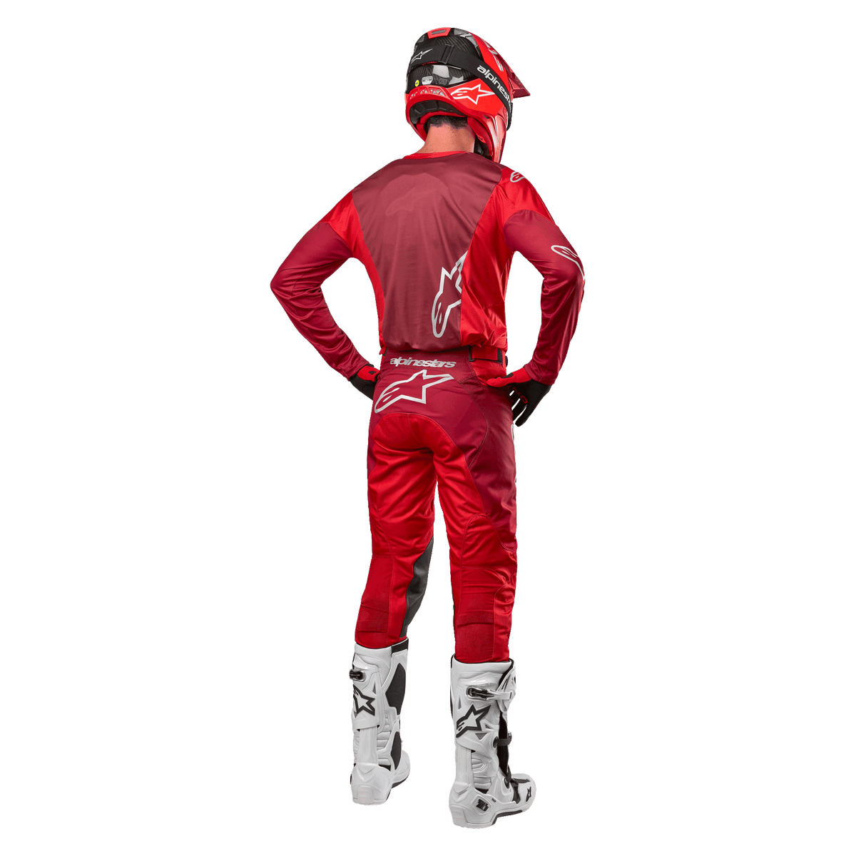Alpinestars 2024 Racer Hoen-bukser og matchende trøje i Mars Red Burgundy, set bagfra af en motocross-kører i fuldt udstyr inklusiv rød hjelm og hvide støvler, der viser den atletiske pasform og branding til off-road kørsel.
