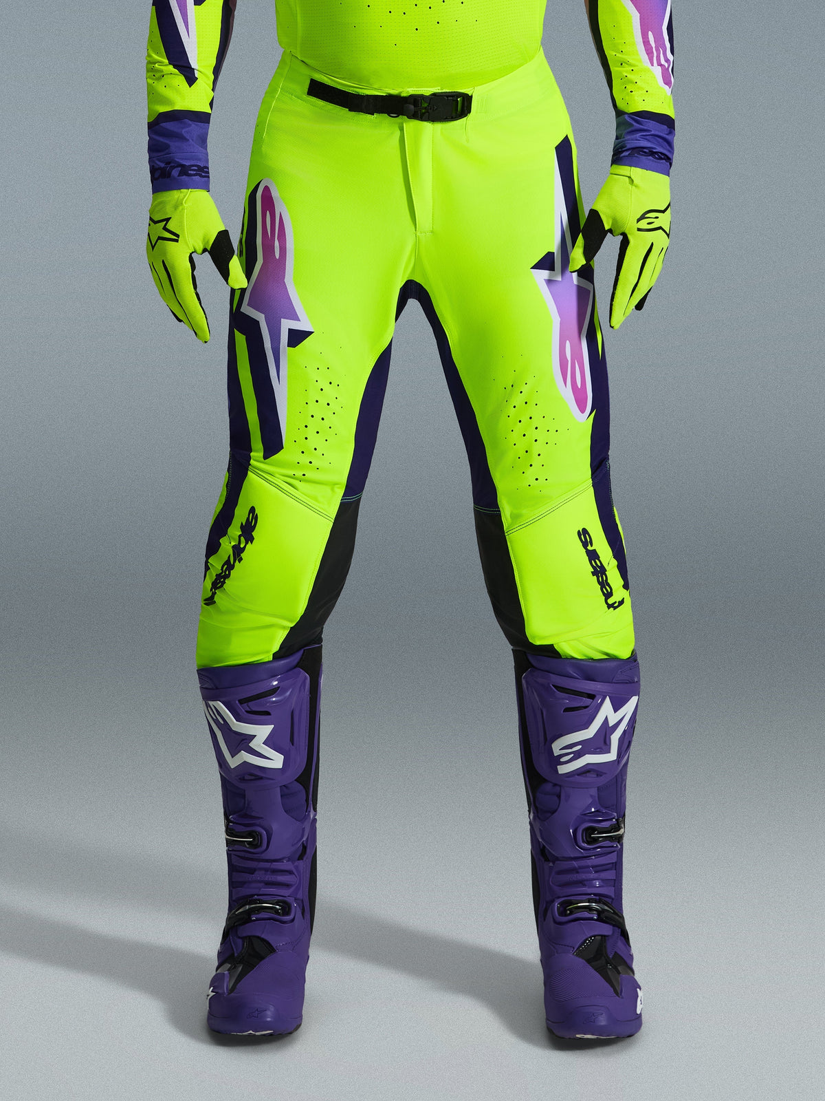 Alpinestars 2026 Supertech Vista Pants, Motocross Pants, Fluorescent Yellow Purple and Black, worn with matching gloves and purple boots, featuring large gradient logos on thighs, perforated zones for ventilation, and a professional athletic design for off-road racing