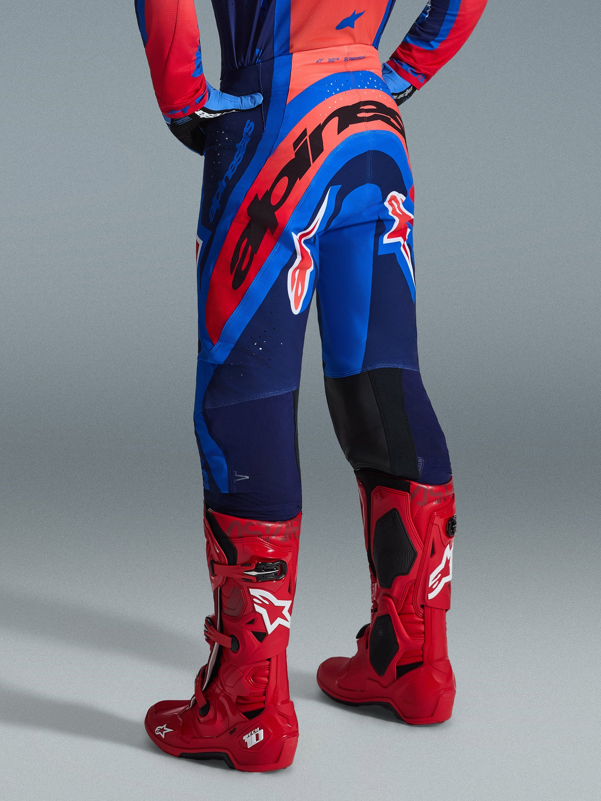 Alpinestars 2026 Supertech Vista bukser, motocrossbukser, Dark Navy Hot Coral Cobalt, set bagfra med markant rød Alpinestars-branding på bagen, kombineret med klare røde motocrossstøvler, letvægts strækkonstruktion til professionel racing