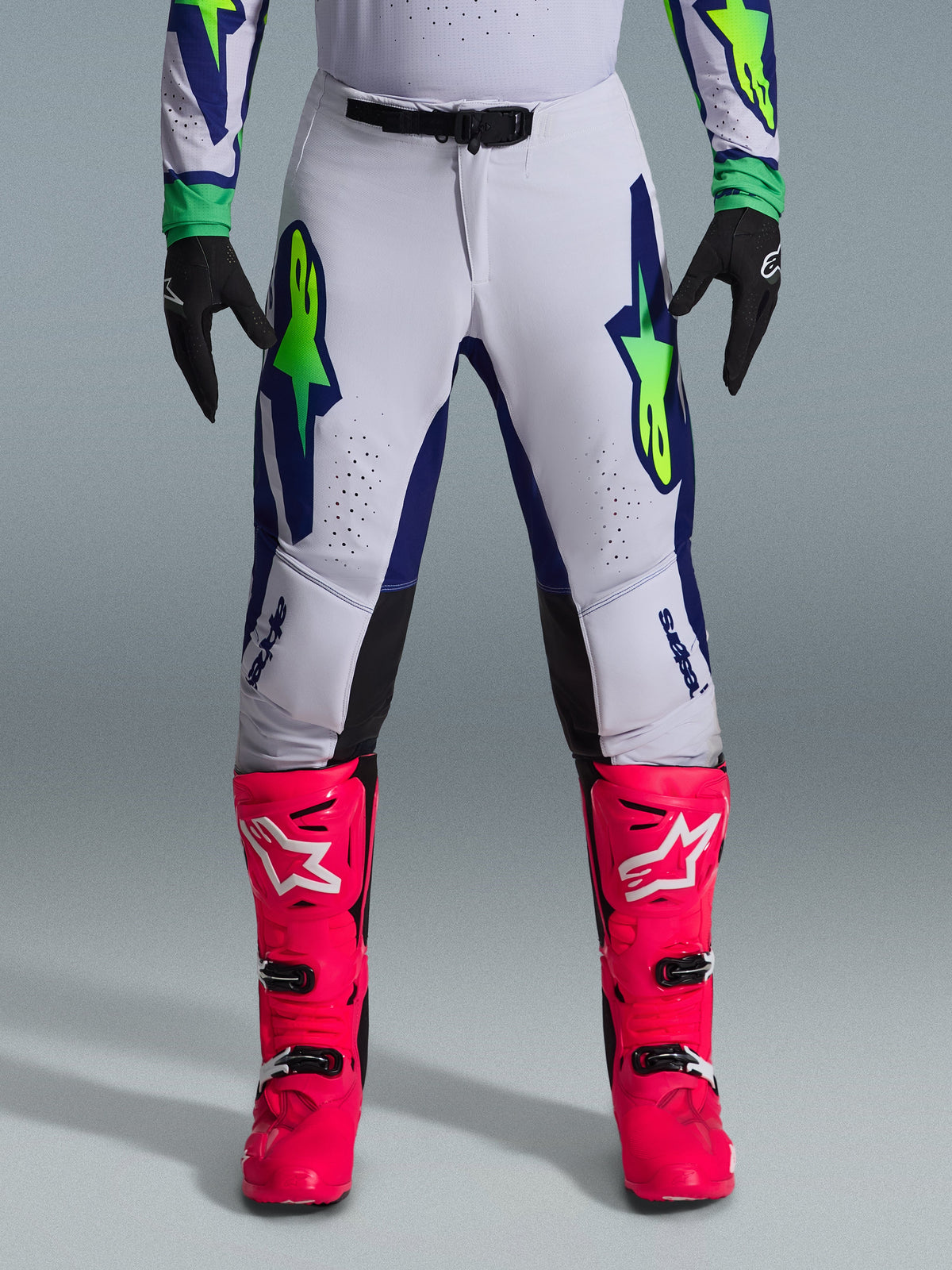 Alpinestars 2026 Supertech Vista-udstyrssæt, motocross-bukser i hvid med blå og limegrønne detaljer, parret med livlige lyserøde støvler og sorte handsker, professionelt racerudstyr med atletisk pasform og laserudskårne perforeringer.