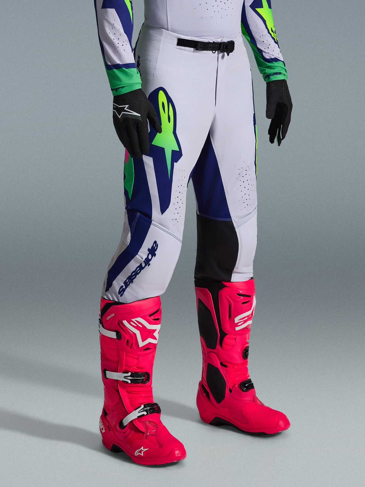 Alpinestars 2026 Supertech Vista bukser, motocrossbukser, lysegrå med neongule og blå detaljer, båret med iøjnefaldende pink motocrossstøvler og sorte handsker, atletisk race-pasform med holdbar strækkonstruktion til elite terrænkørsel