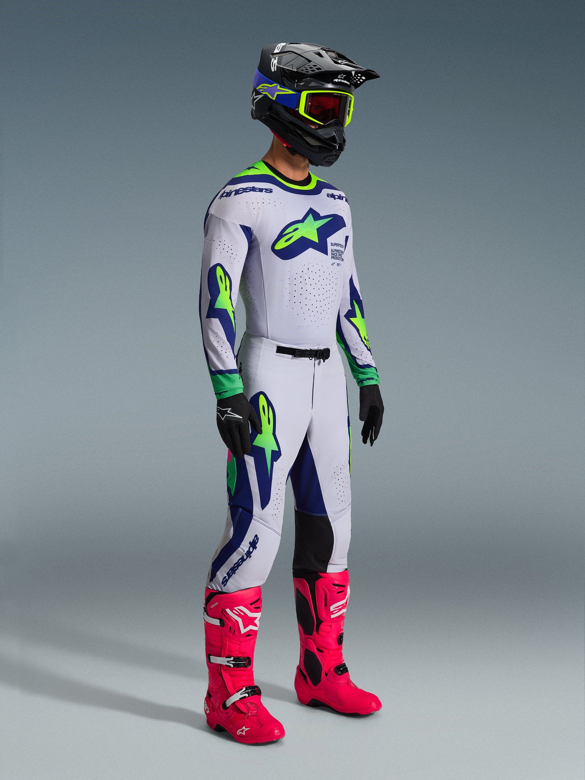 Alpinestars 2026 Supertech Vista bukser og matchende trøje, motocross-udstyr i lysegrå med gul fluo og blå detaljer, båret af en kører med sort hjelm og stærke lyserøde støvler, dristig atletisk grafik og professionel racer-pasform
