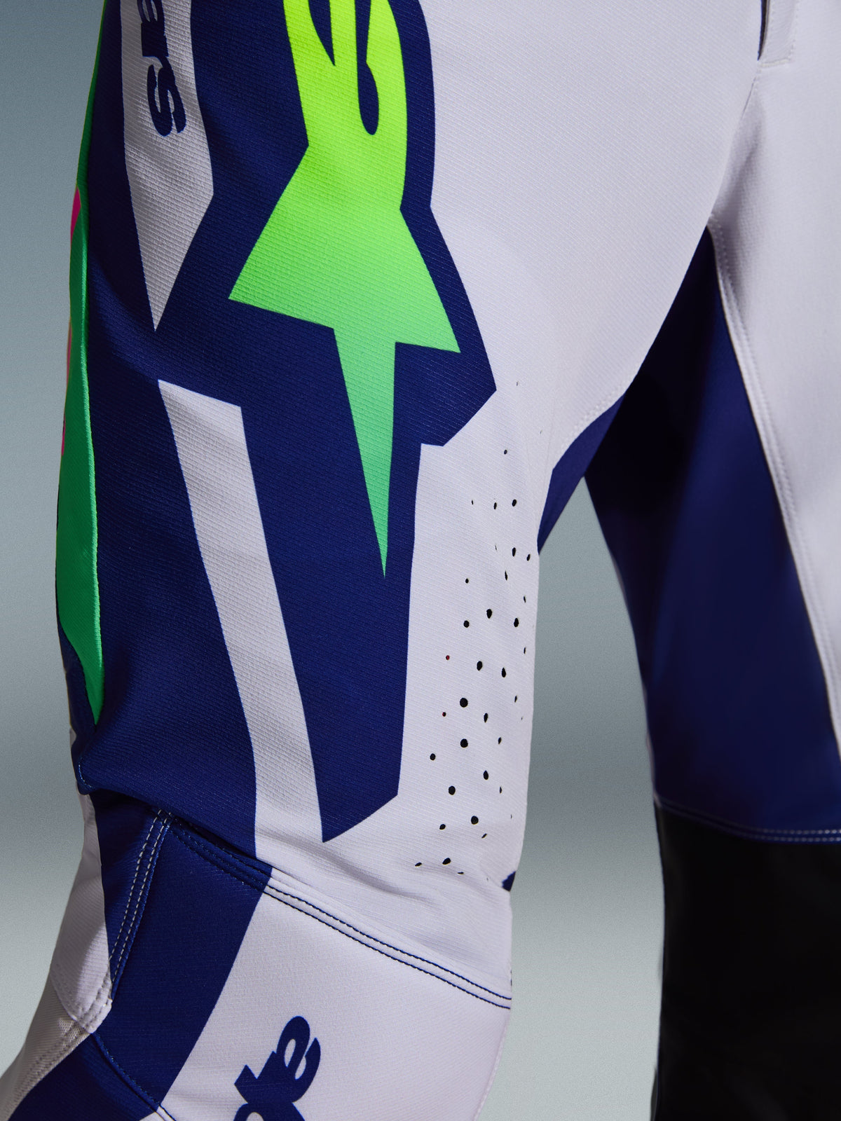Alpinestars 2026 Supertech Vista bukser, motocrossbukser, lysegrå med Yellow Fluo og blå detaljer, nærbillede af låret der viser det store A-star logo, laserskårne ventilationshuller og avanceret stræk-ripstop-stof.